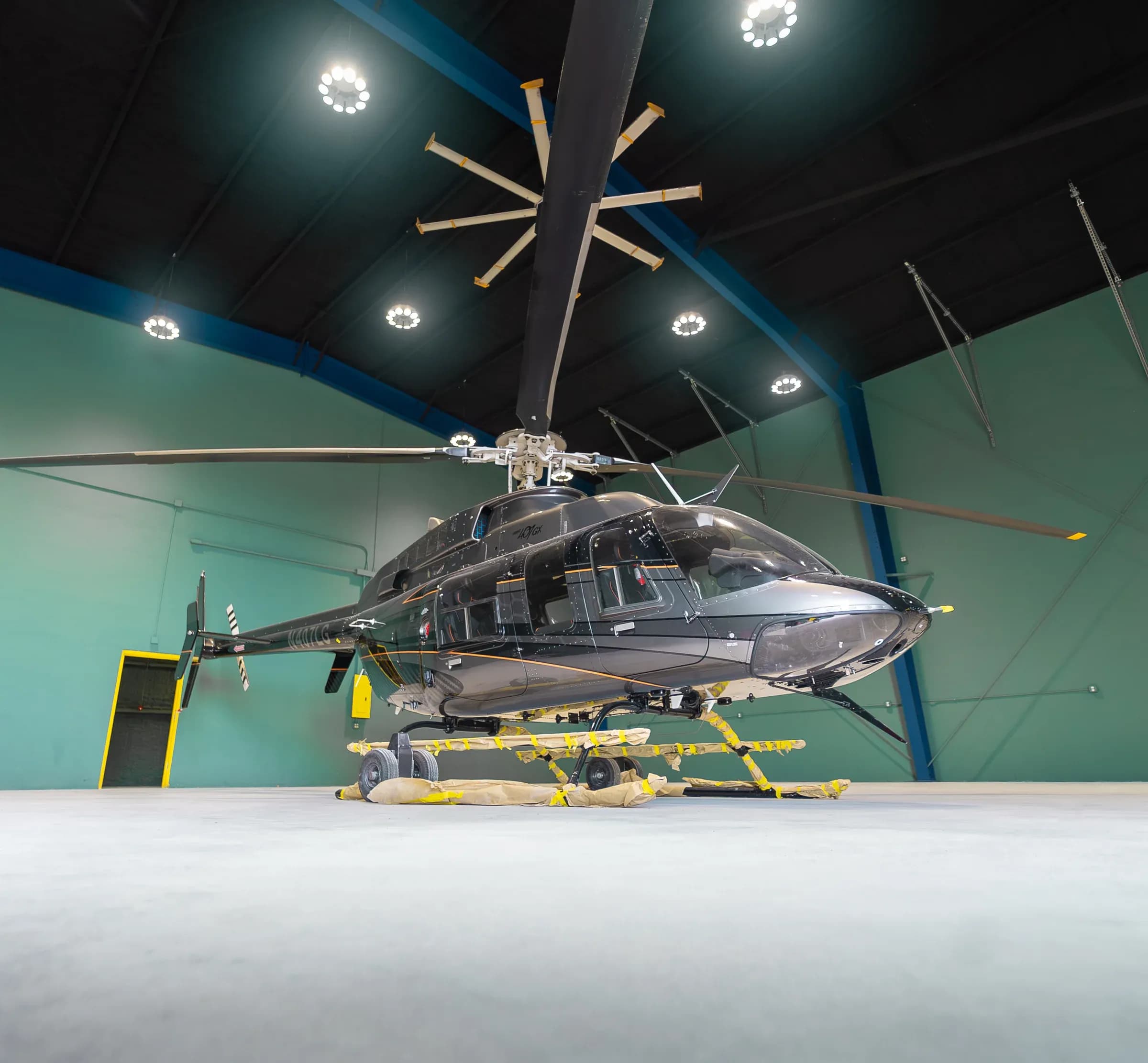 Low frontal view of the Bell 407 inside a hangar beneath the roof structure.
