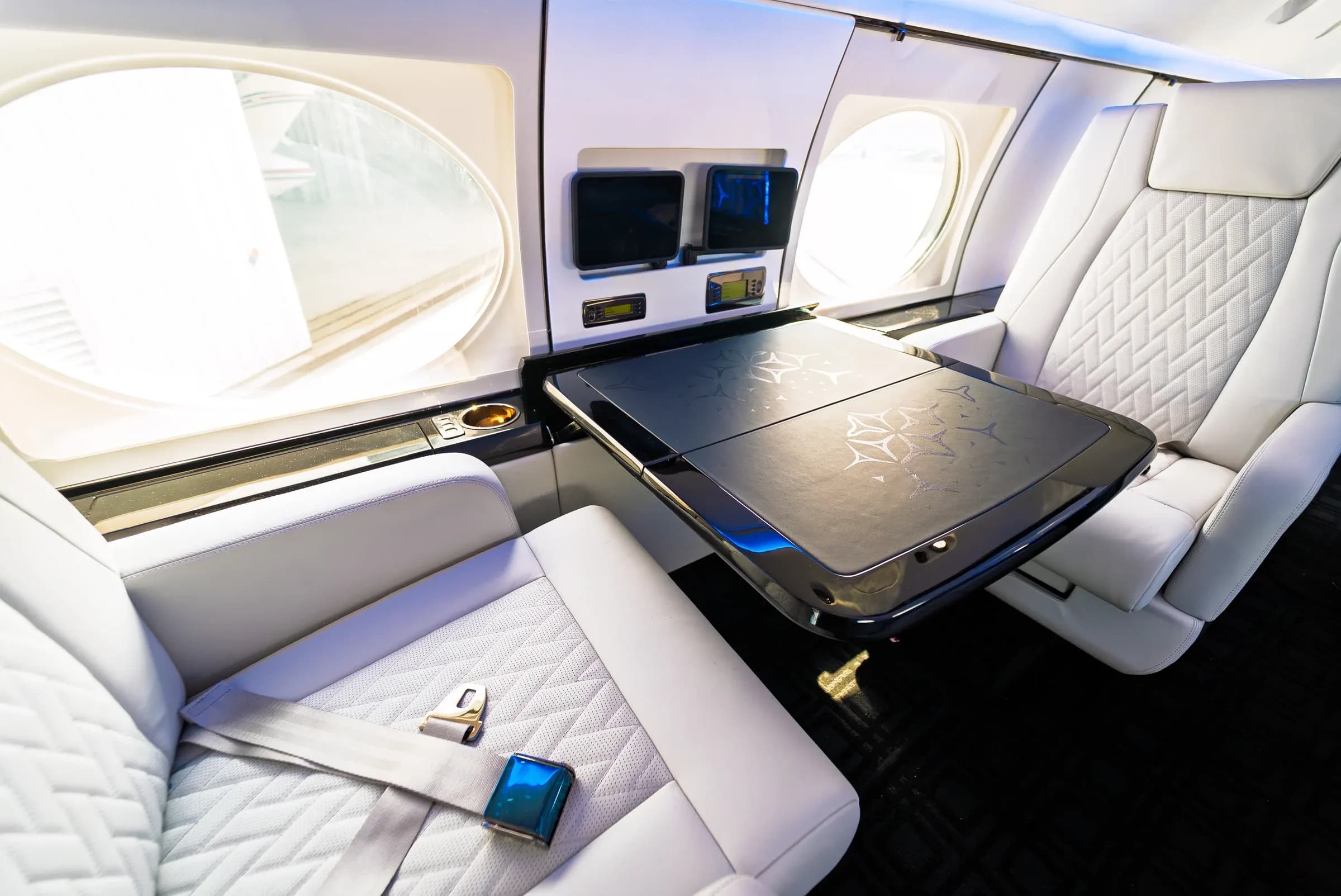 Angled view of Gulfstream G-IV club seats and a dark table with geometric detailing and blue edge lighting.