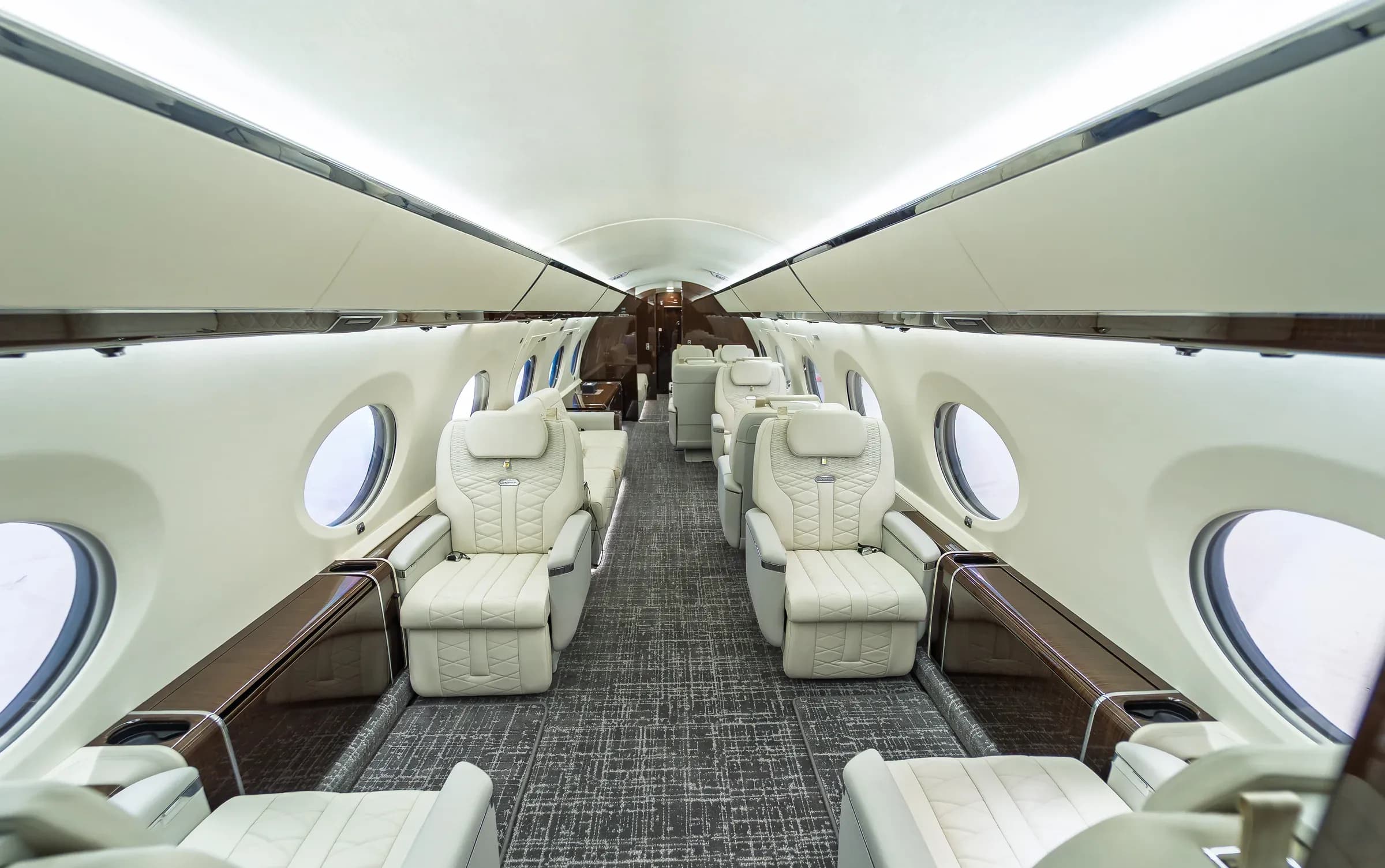 Centered Gulfstream G650ER cabin view with ivory quilted seats, glossy wood side ledges and gray patterned carpet.