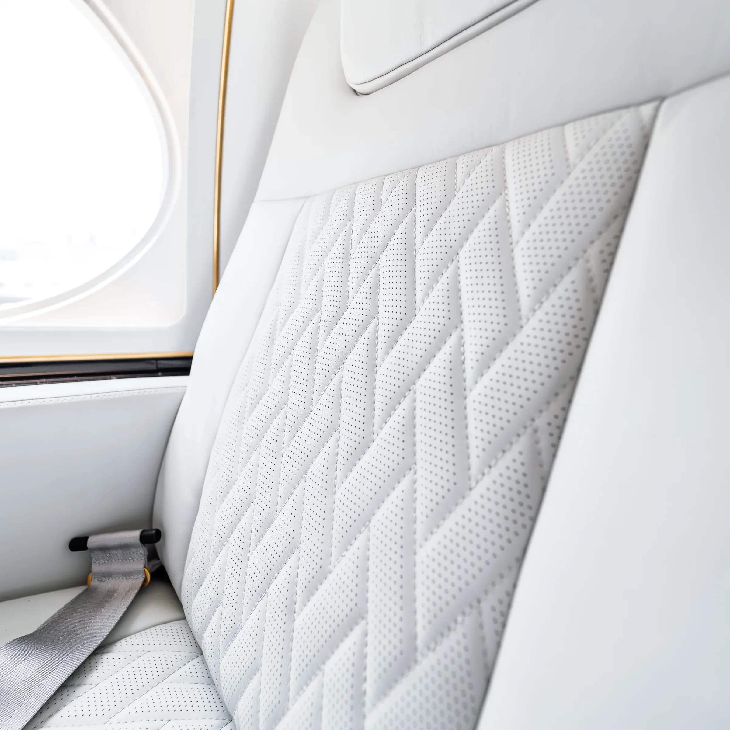 Close view of perforations and diamond stitching on white Gulfstream G550 upholstery.
