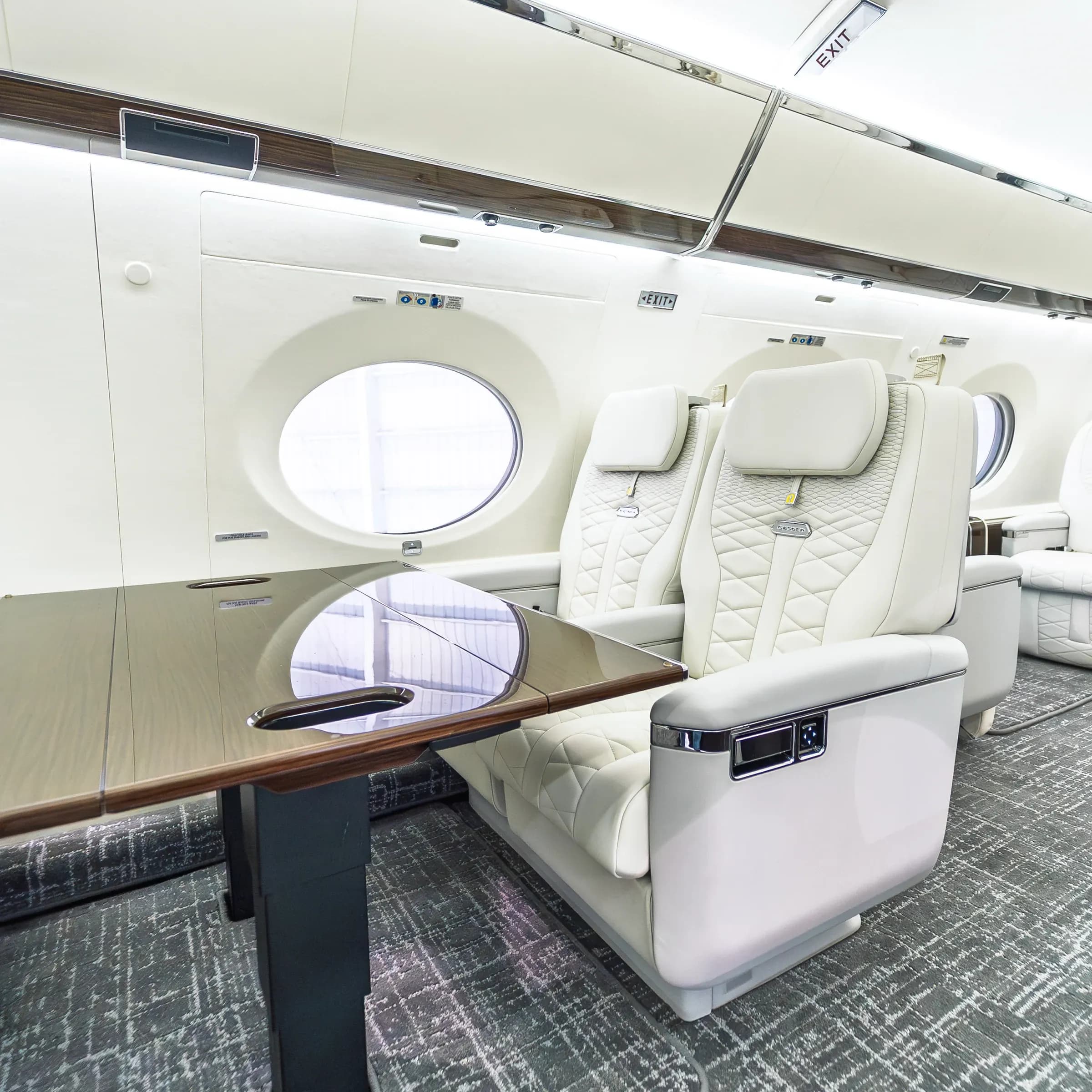 Ivory Gulfstream G650ER chair beside a glossy wood table and oval window.