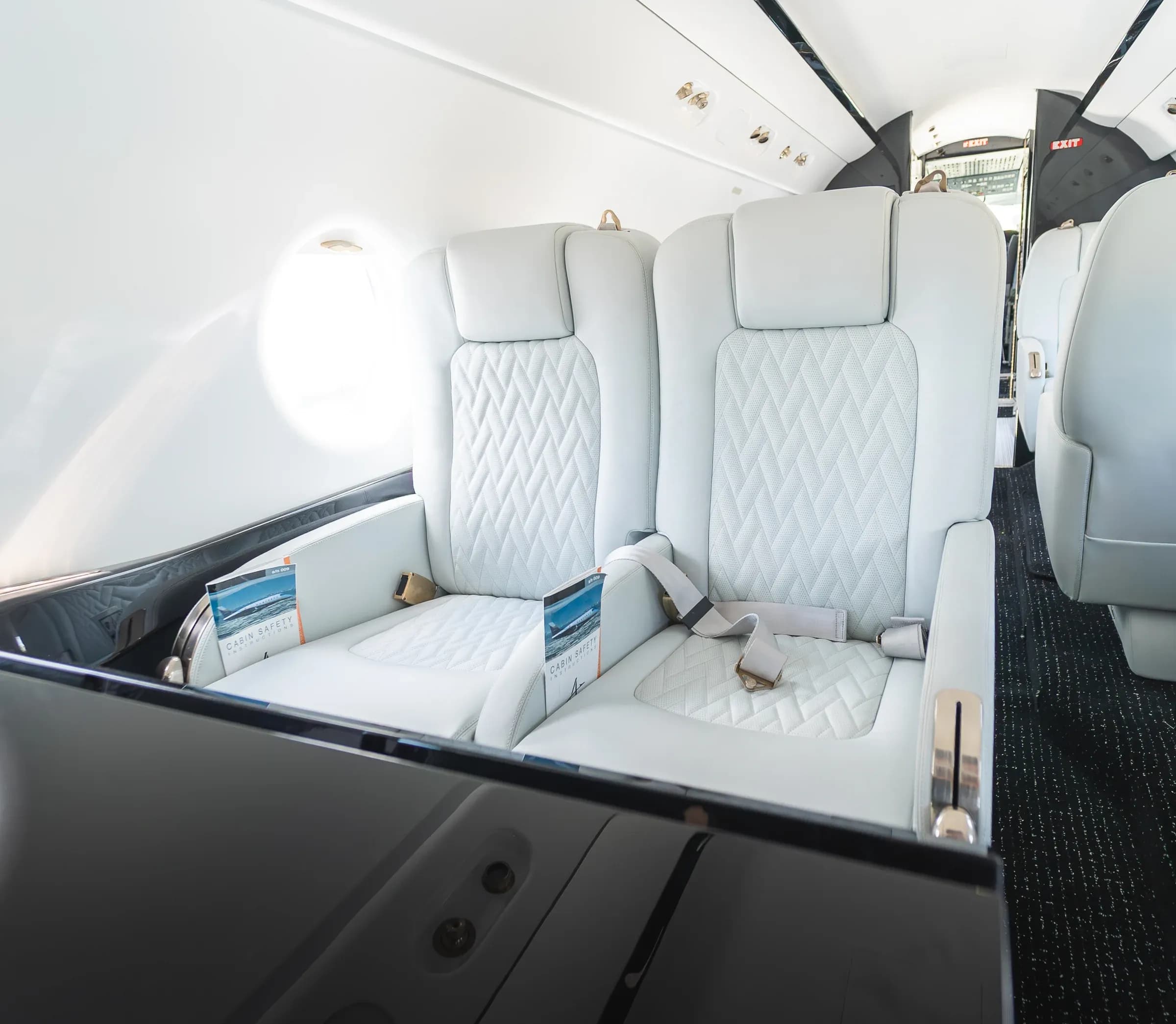 Two white quilted Gulfstream G200 seats behind a glossy dark cabin table.