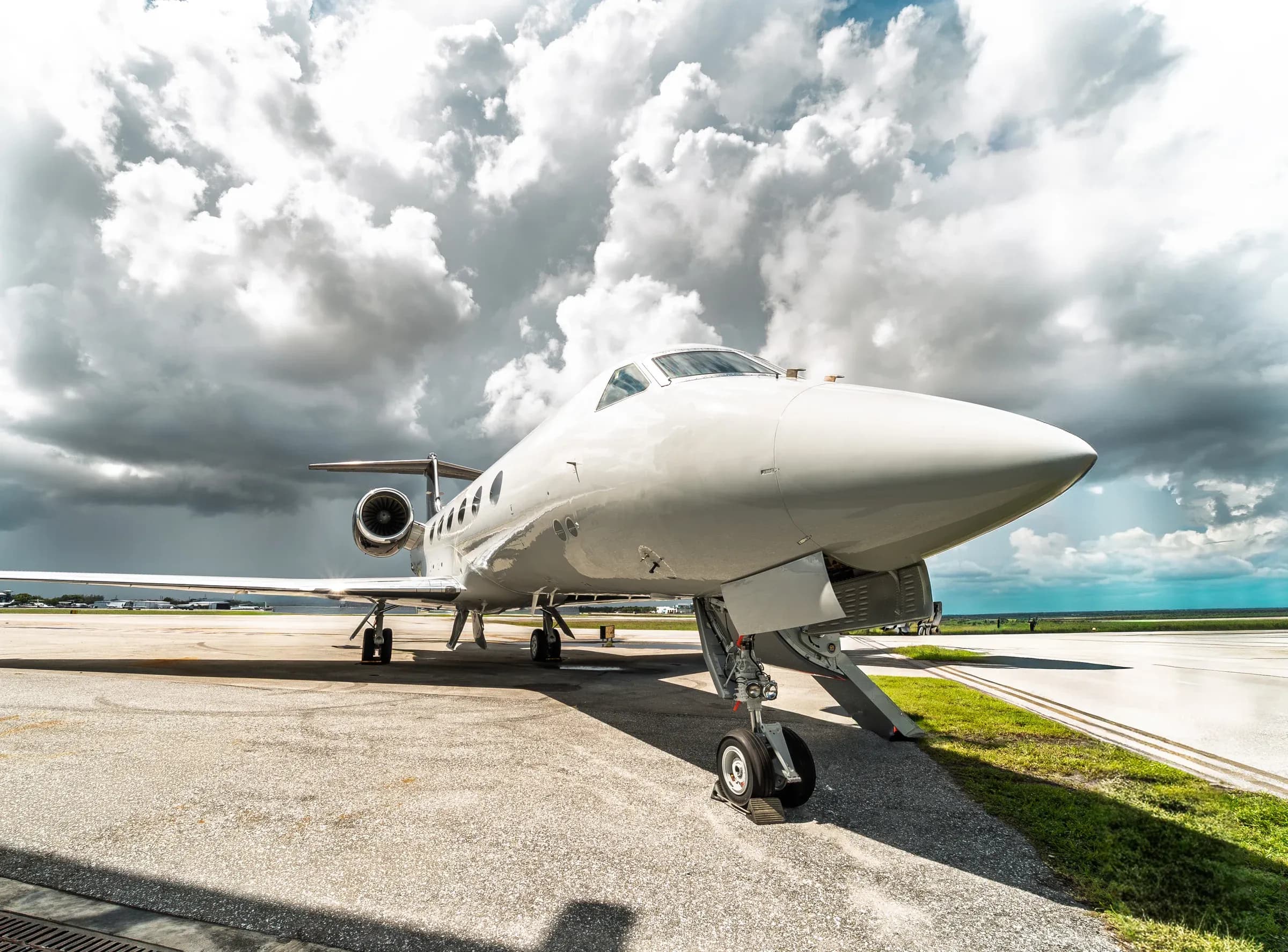 Front three-quarter view of the white Gulfstream G-IV beneath dramatic clouds.