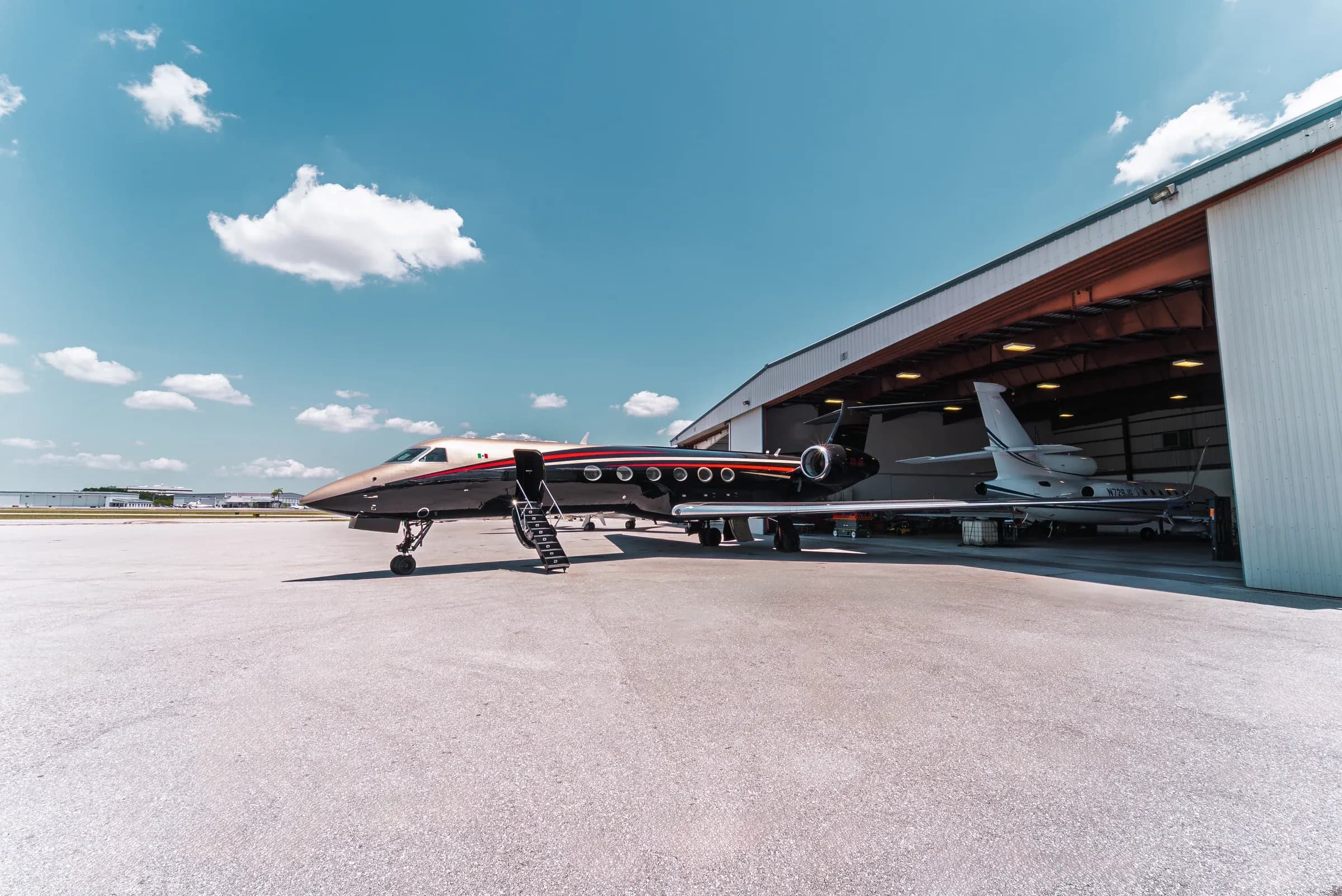 Wide view of the Gulfstream G550 nose and fuselage beside a hangar under a blue sky.