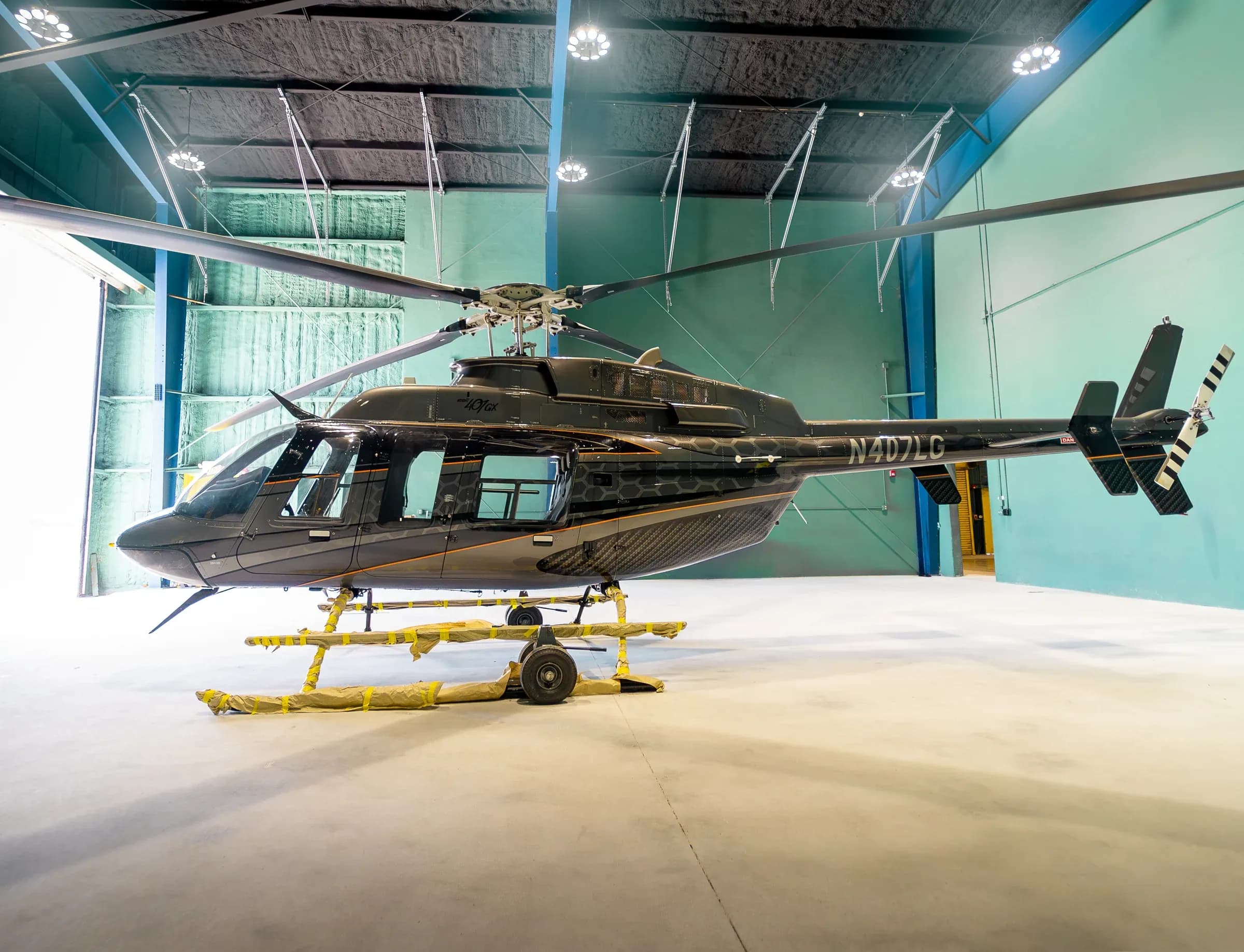 Full side profile of the Bell 407 inside a hangar with ground handling equipment.