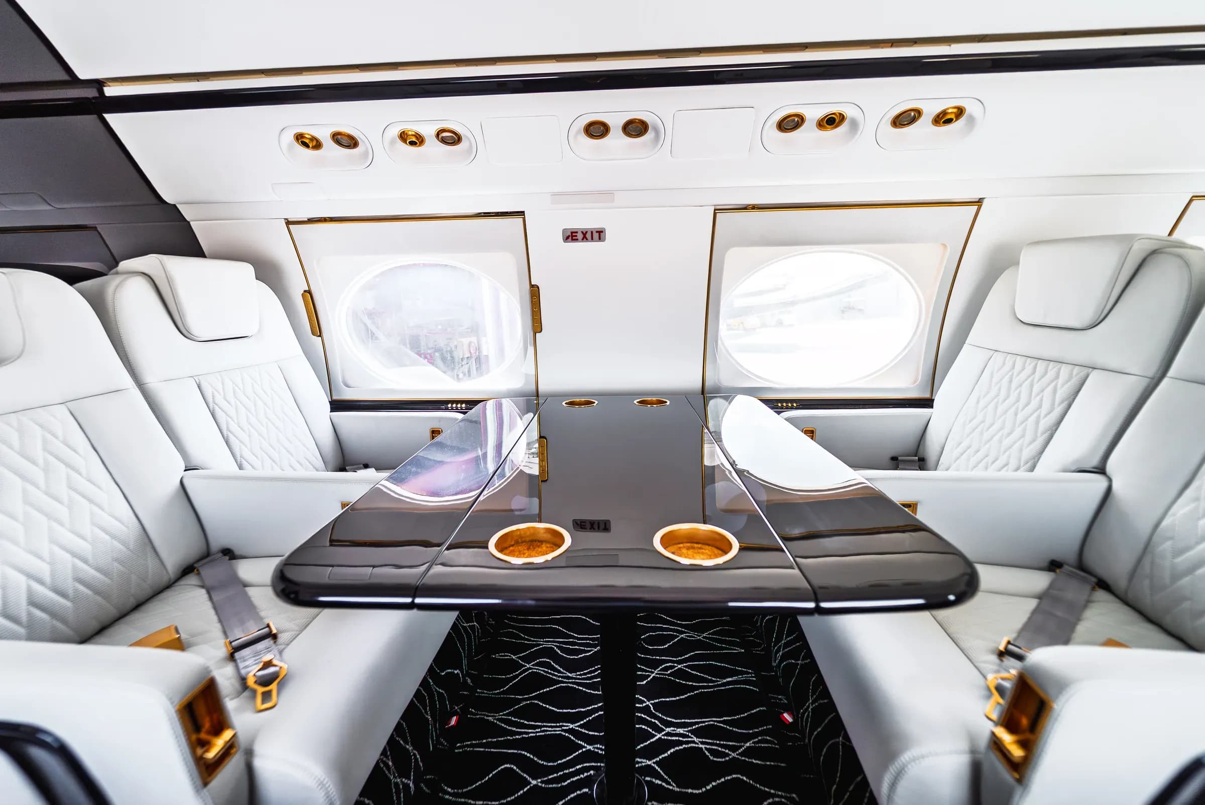 Facing Gulfstream G550 club seats around a glossy dark table with gold-tone cup holders.