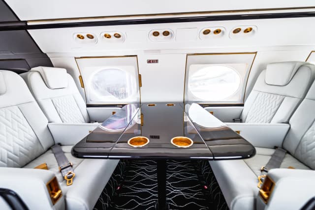 Facing Gulfstream G550 club seats around a glossy dark table with gold-tone cup holders.