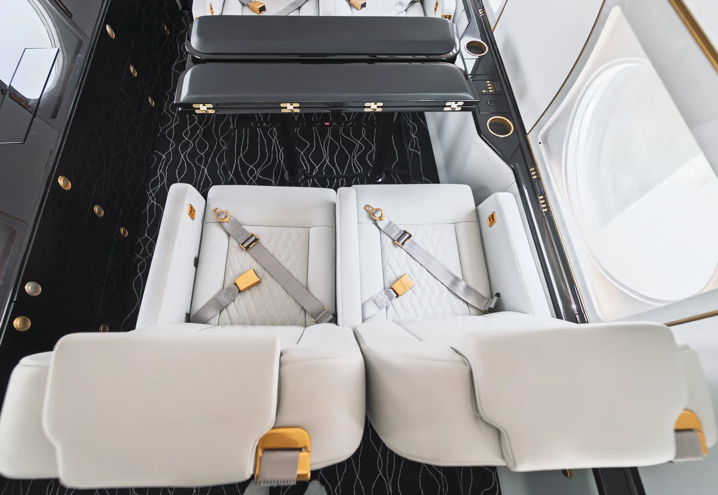 Overhead view of white quilted Gulfstream G550 seat cushions and gold-tone seat belt fittings.