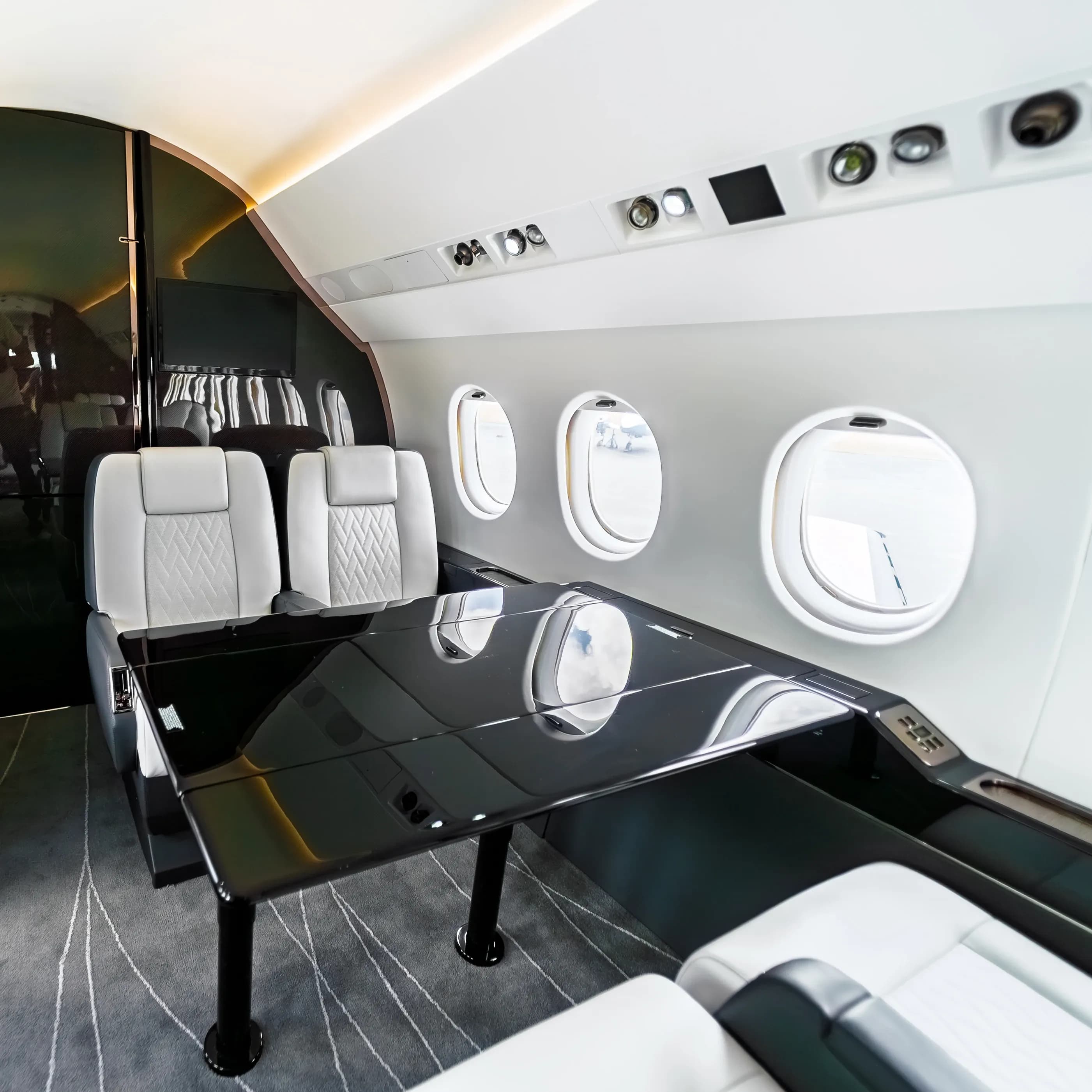 Glossy dark Falcon 2000 cabin table between quilted seats beside the oval windows.