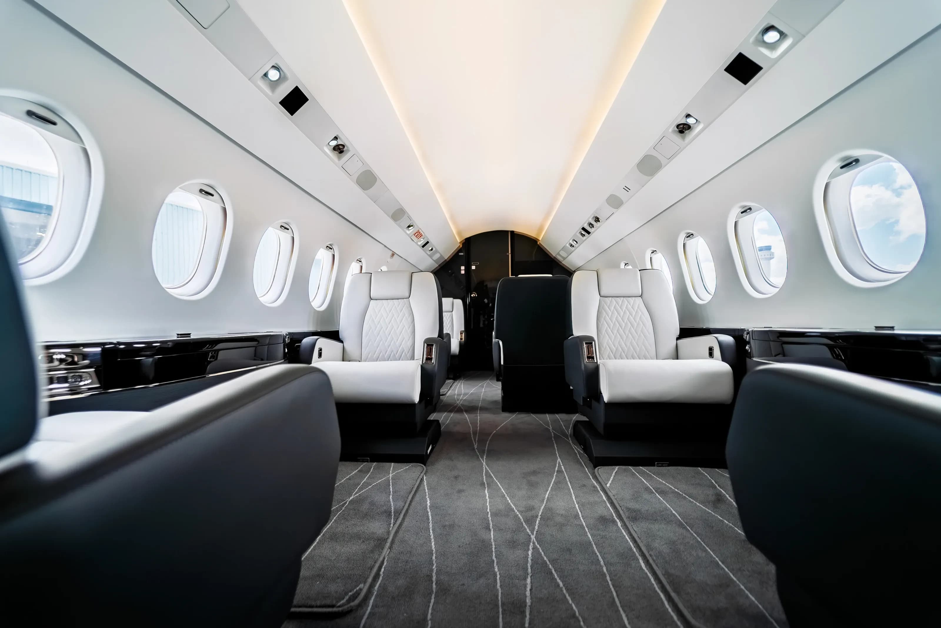 Low view through the Falcon 2000 cabin with light seats, dark surrounds and flowing carpet lines.