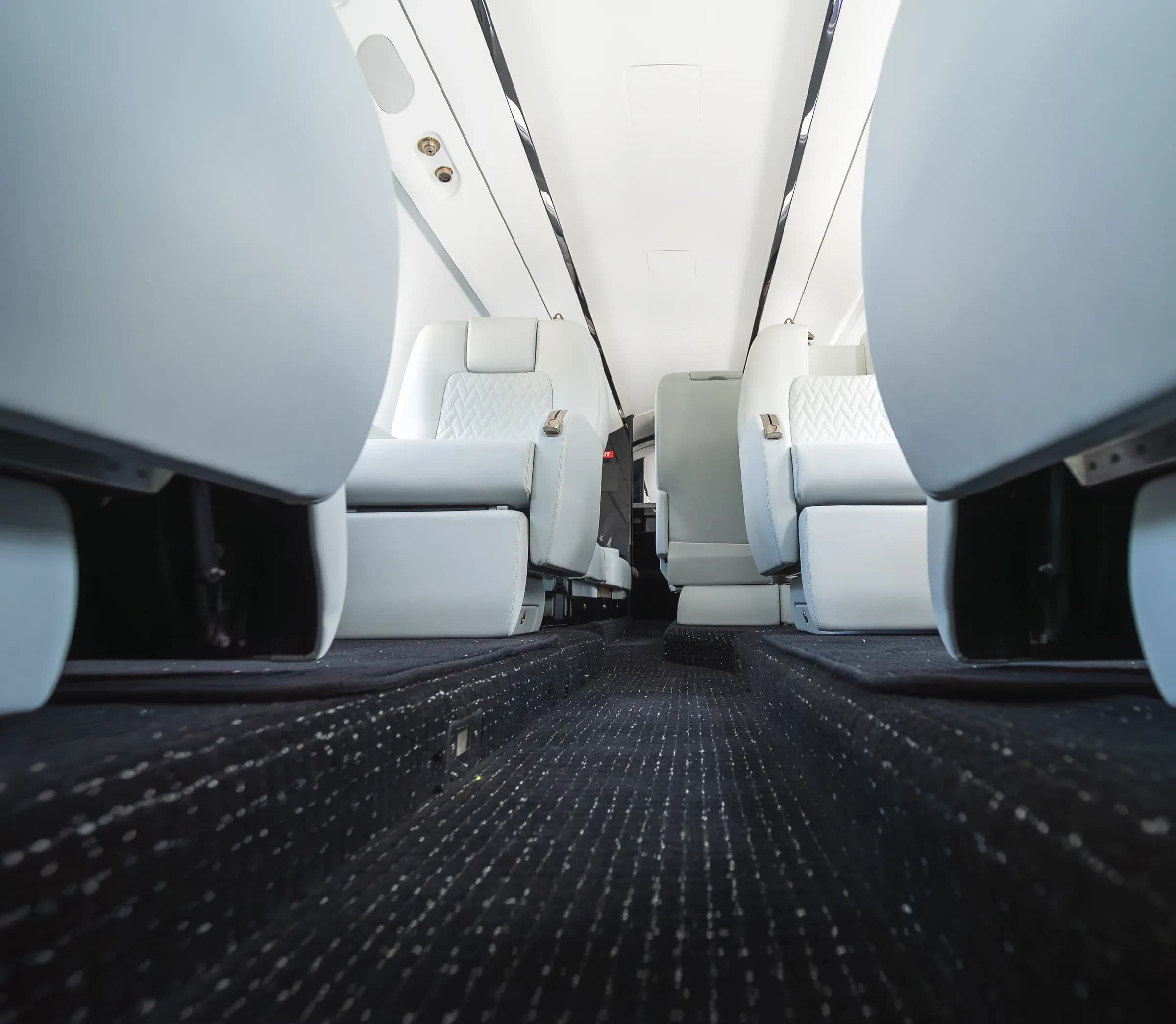 Low view along the Gulfstream G200 aisle, showing patterned carpet and the bases of the white seats.