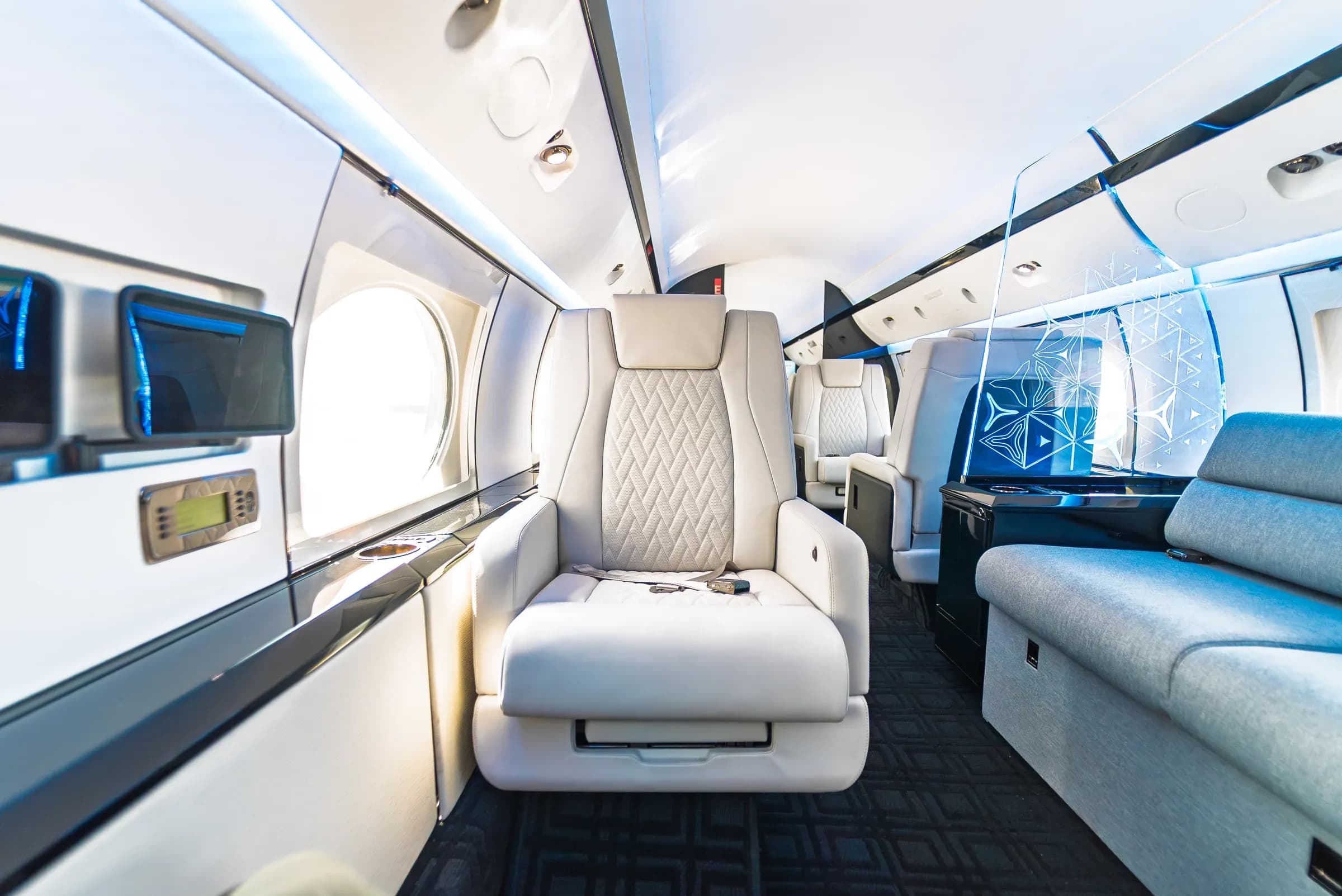 White Gulfstream G-IV seat beside the blue divan and illuminated cabin partition.