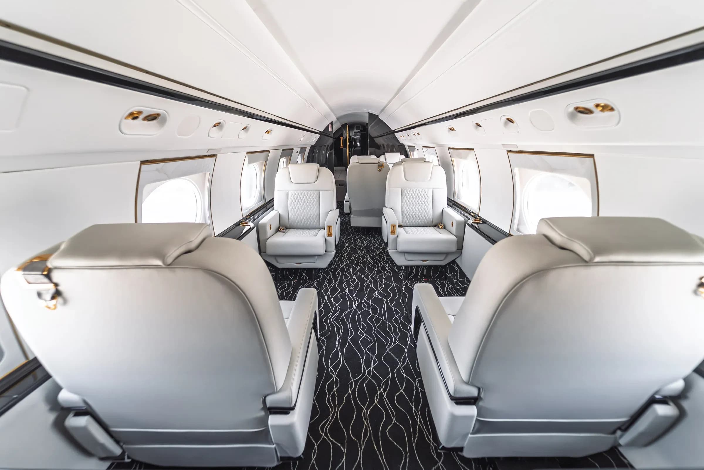View along the Gulfstream G550 cabin, with white quilted seats and a wavy patterned carpet.