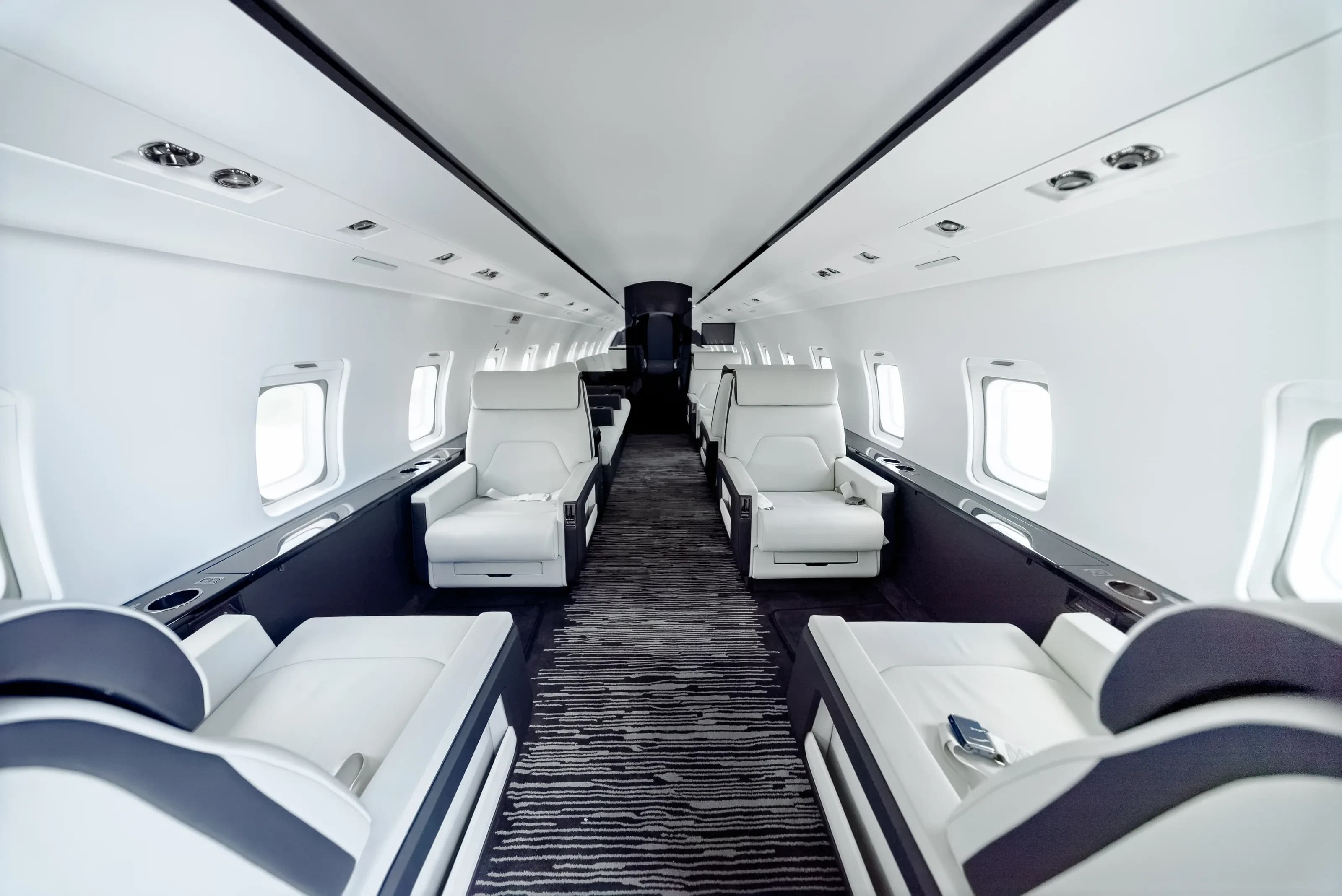 Full Challenger 604 cabin with facing divans, ivory seats and a dark linear-pattern carpet.