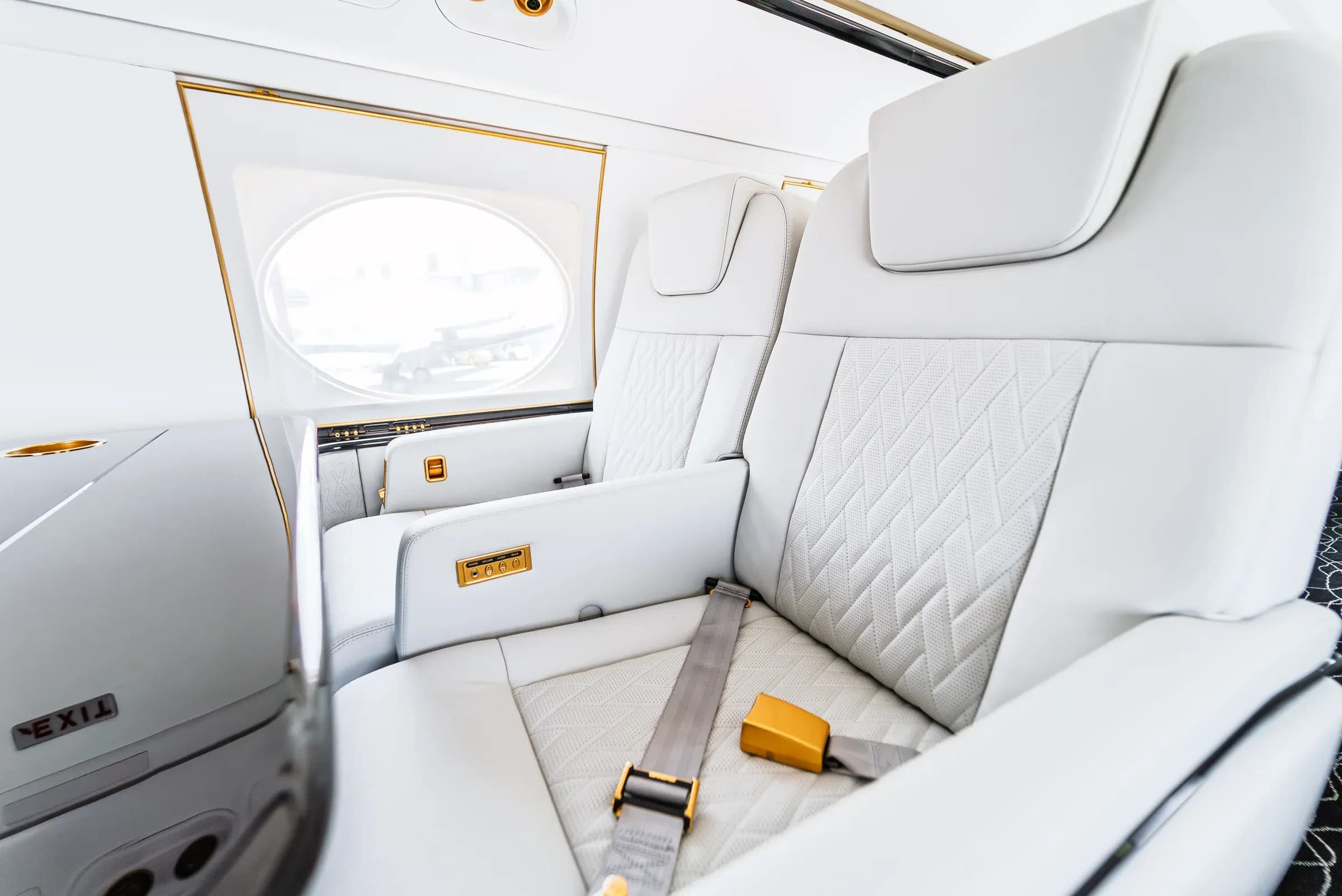 Close view of paired white quilted Gulfstream G550 seats and their seat belts.
