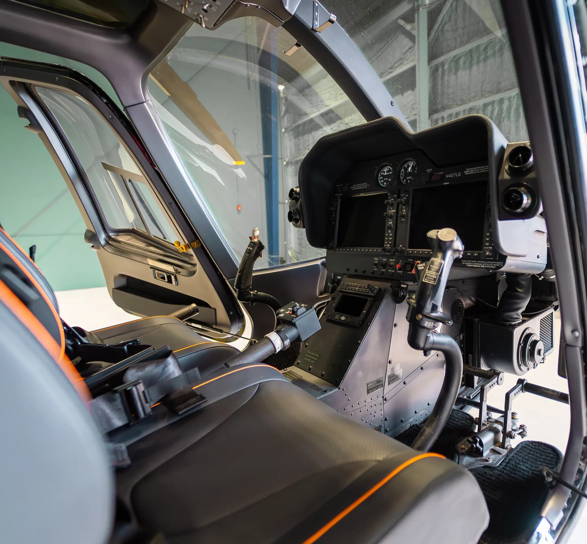 Bell 407 cockpit seat and flight controls with dark upholstery and orange piping.