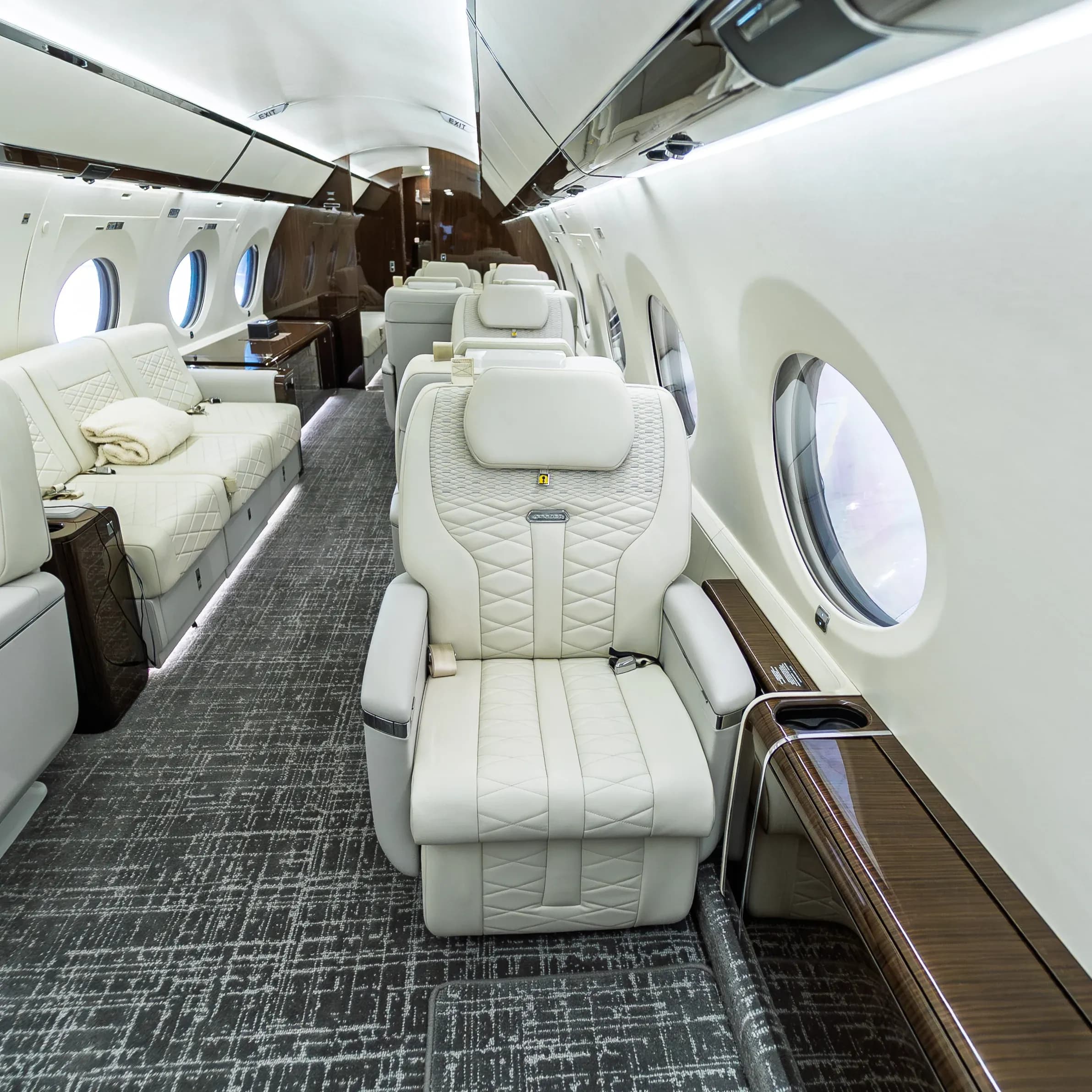 Single ivory Gulfstream G650ER seat beside an oval cabin window.