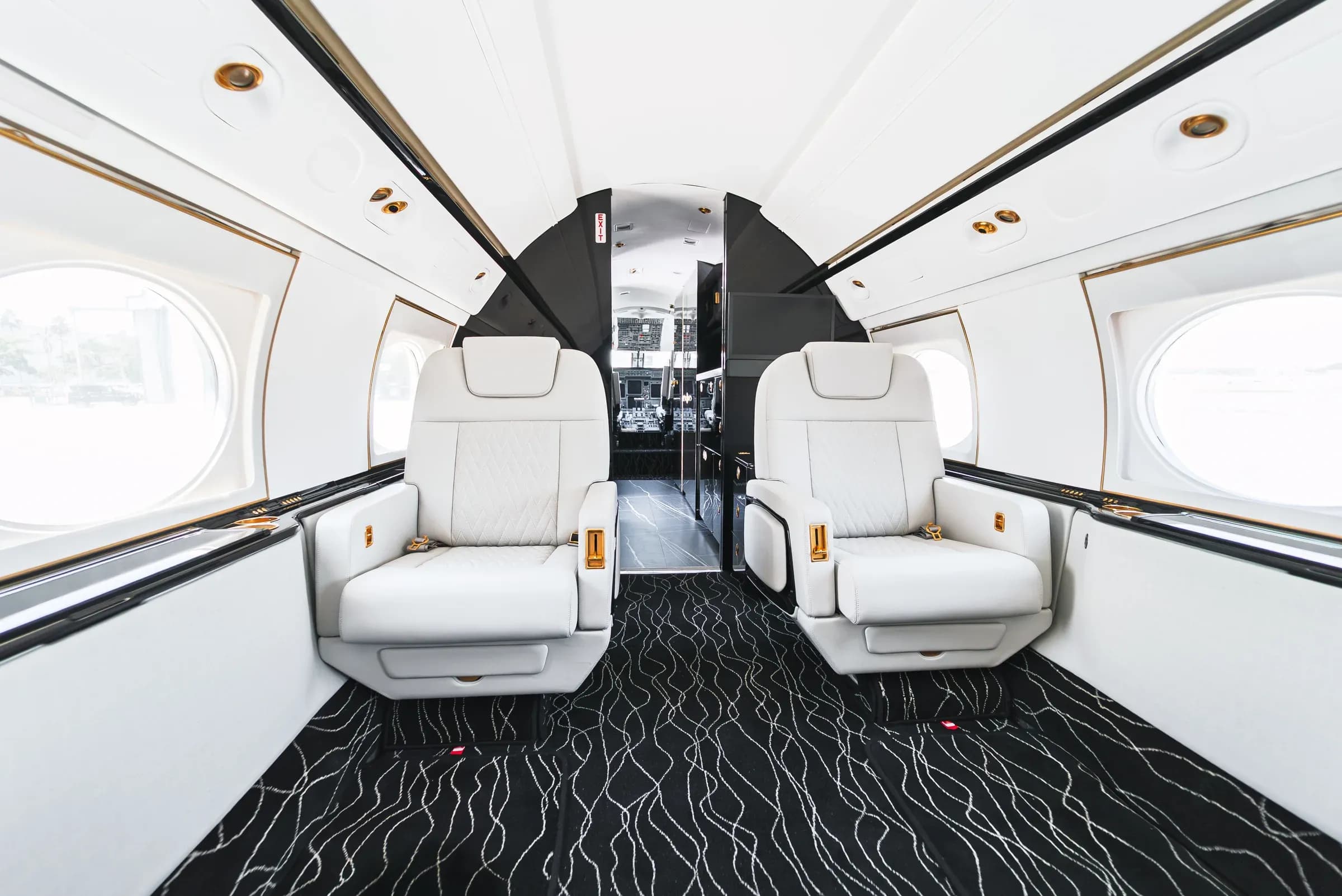 Forward pair of white quilted Gulfstream G550 seats with gold-tone hardware and dark vestibule trim.