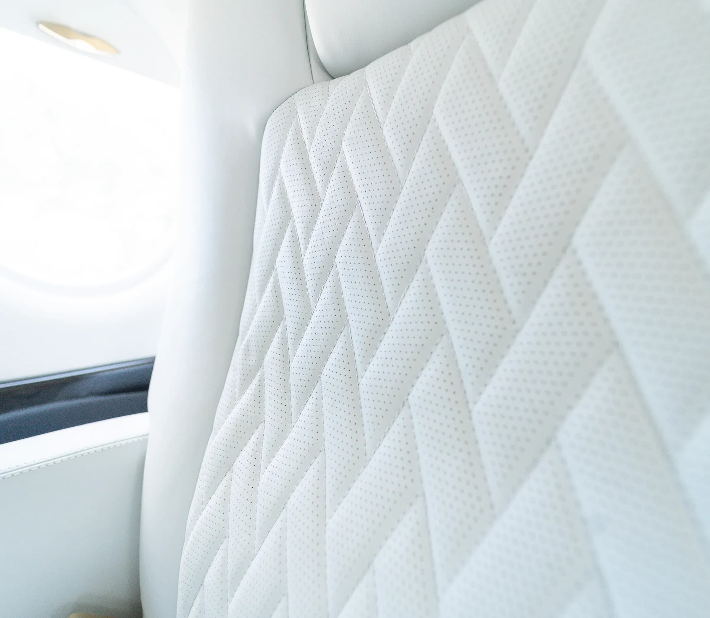 Close view of perforations and diamond stitching on a white Gulfstream G200 seat back.