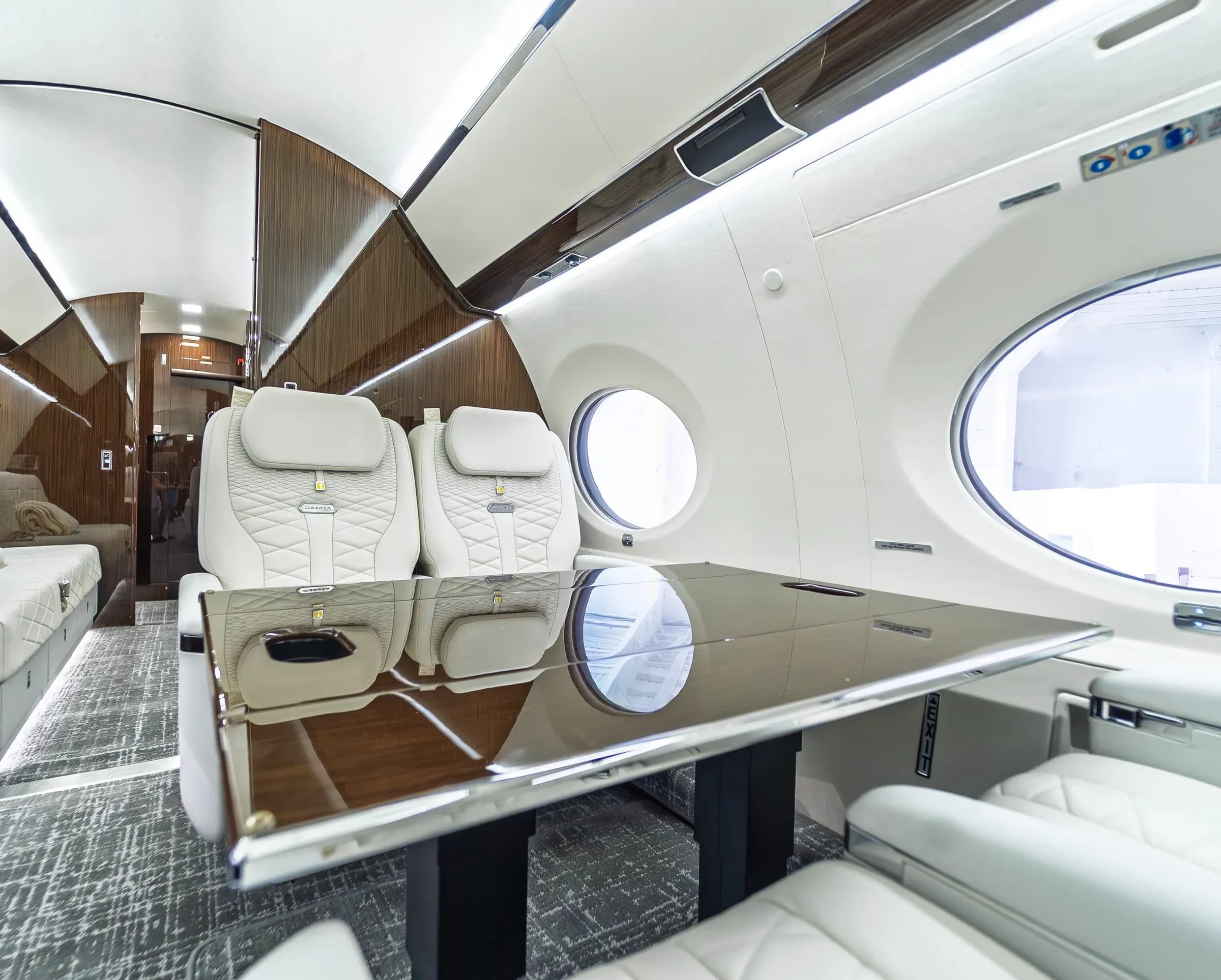 Glossy wood Gulfstream G650ER table with cup holders and reflected cabin windows.