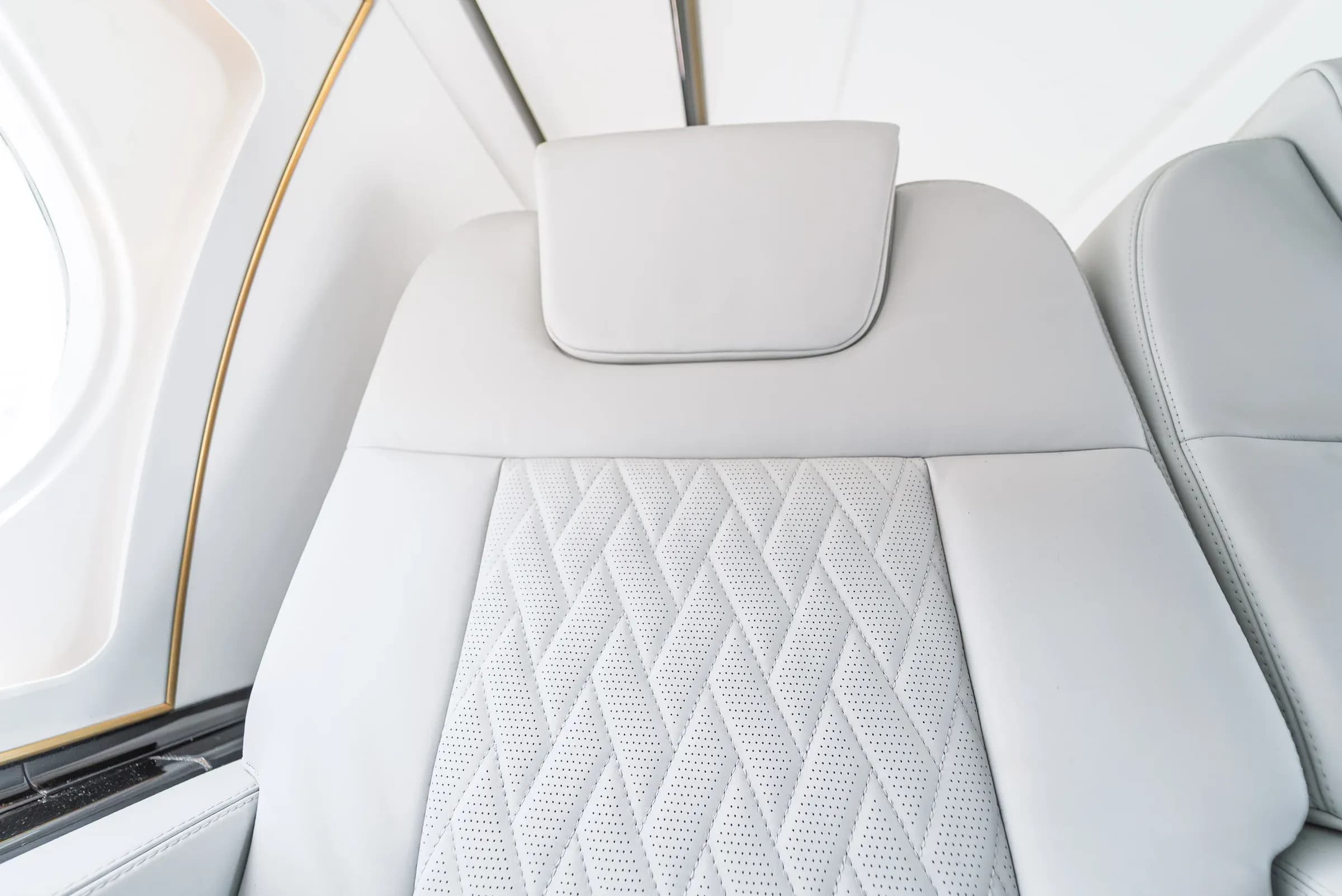 Gulfstream G550 headrest and quilted seat insert beside glossy window trim.