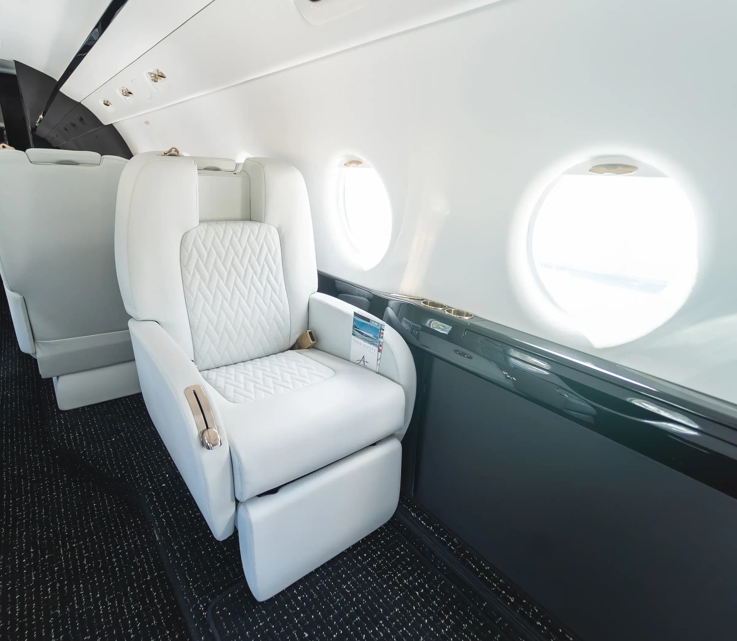White upholstered Gulfstream G200 seat with an extended footrest beside the cabin windows.