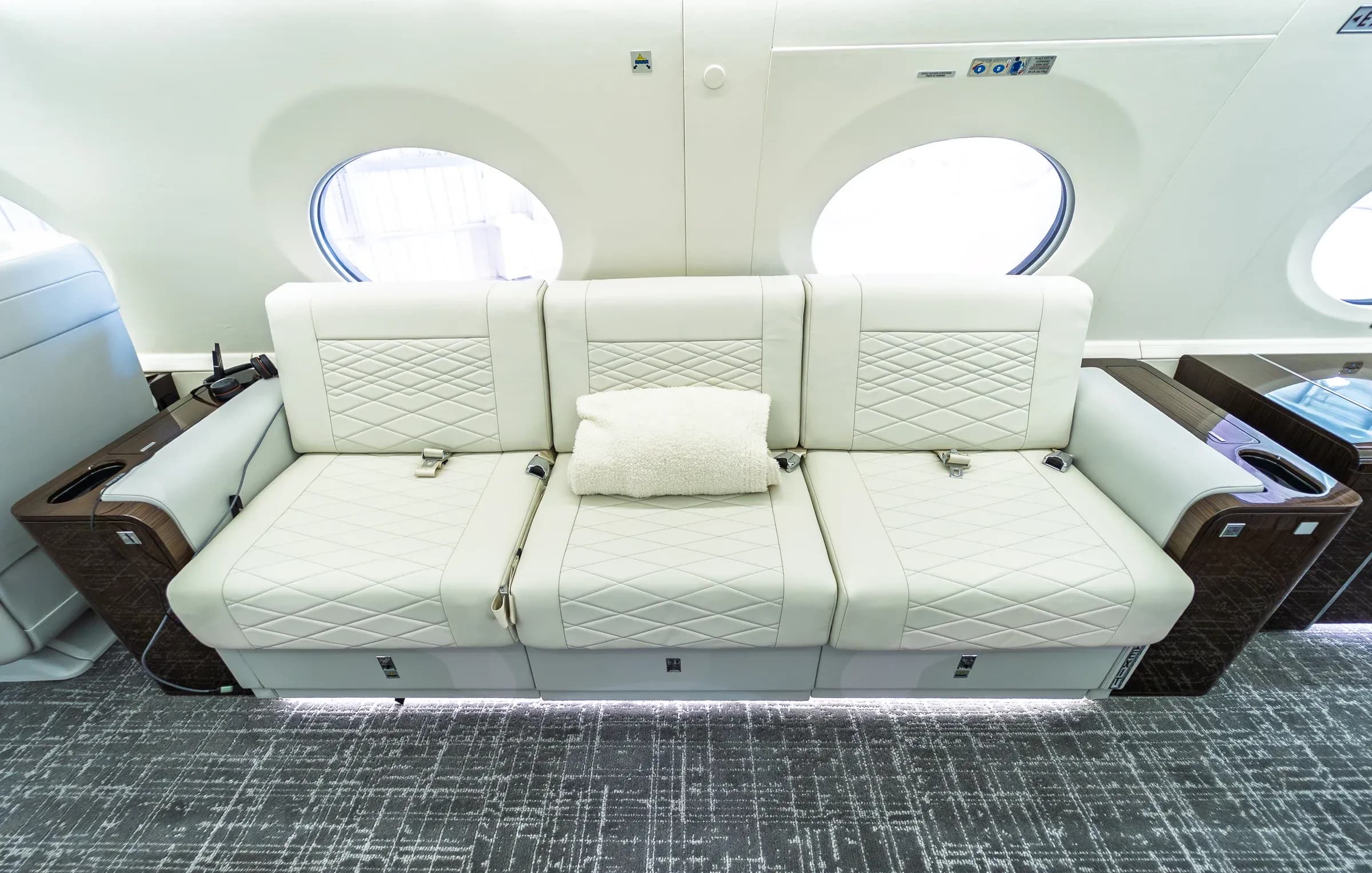 Ivory upholstered Gulfstream G650ER divan with three seat belts below oval windows.