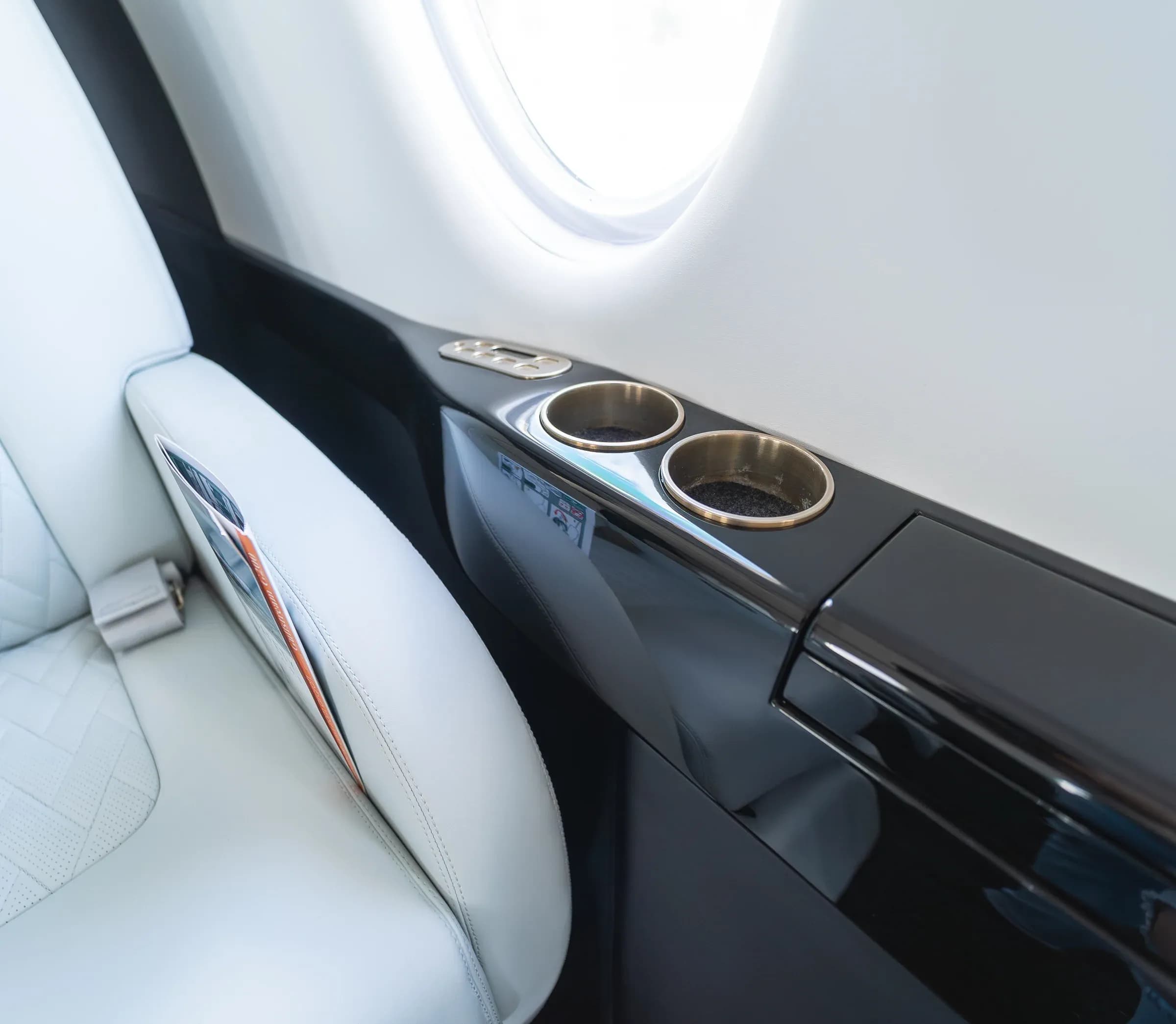 Glossy dark side ledge with cup holders beside a white Gulfstream G200 armrest.