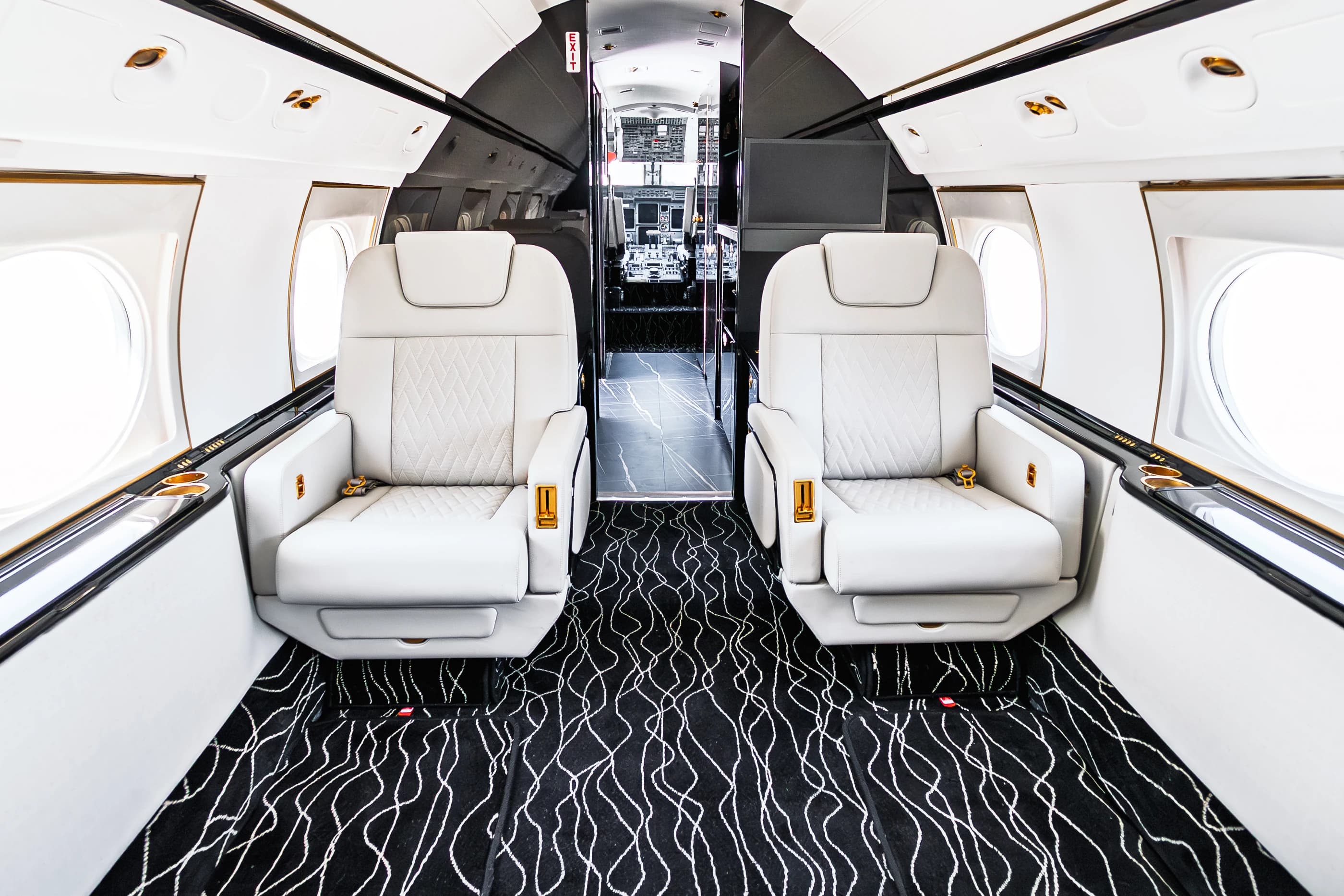 Paired Gulfstream G550 ivory seats, original quilted inserts and a flowing patterned carpet beside the forward cabin entrance.