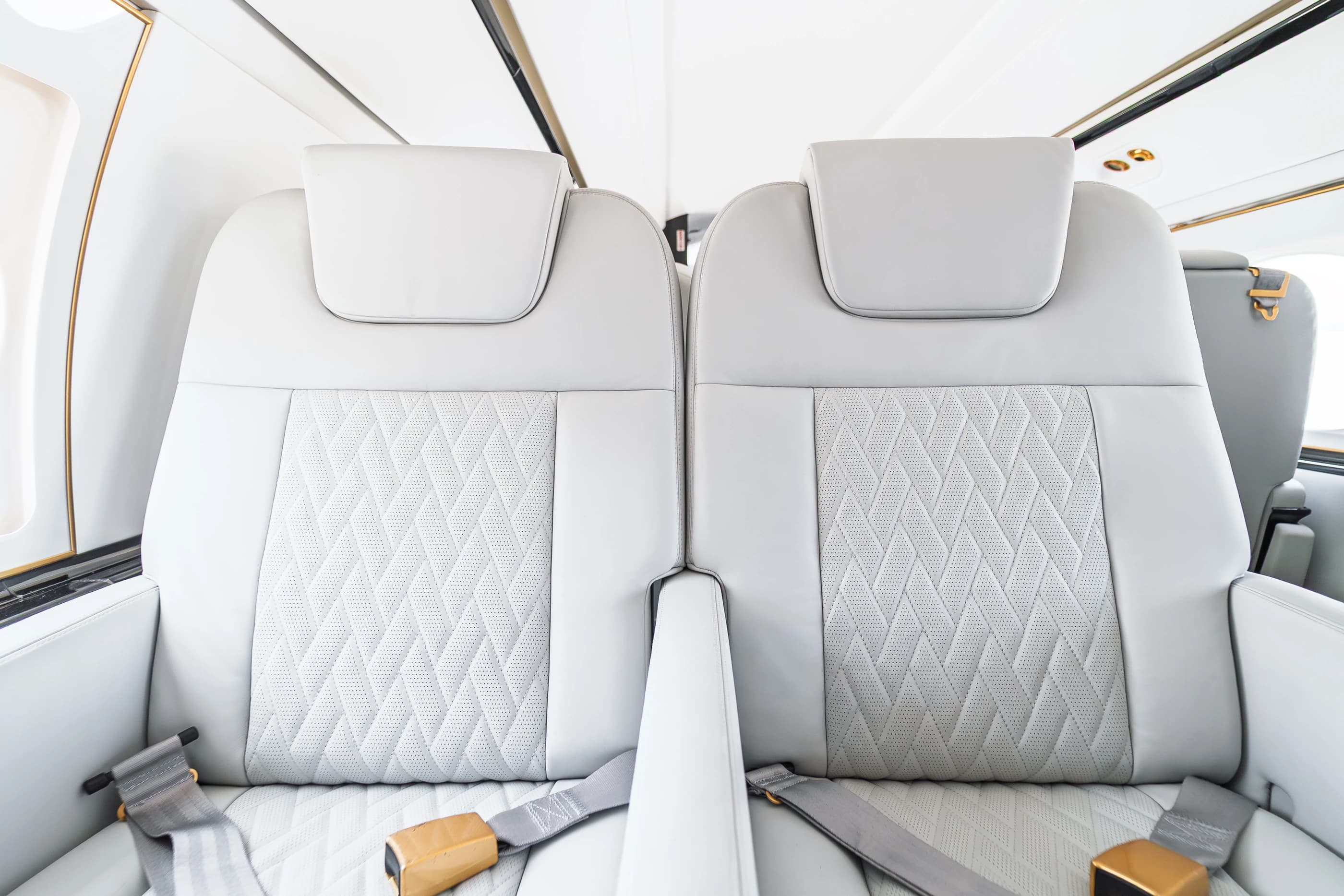 Paired Gulfstream G550 headrests and original perforated upholstery, with tailored stitching and gold-tone seat belt fittings.