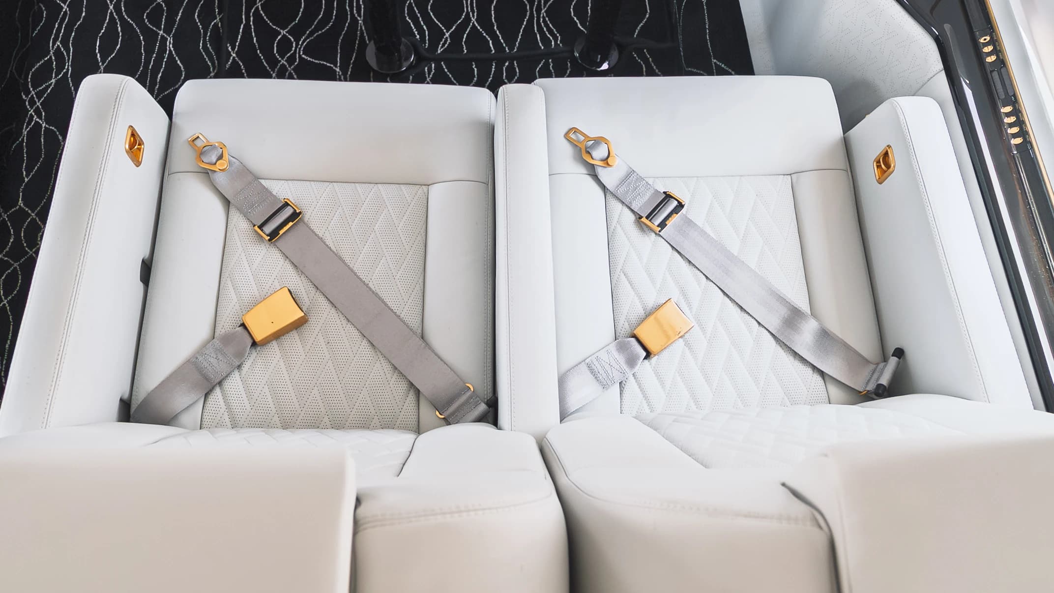 Original gold-tone Gulfstream G550 seat belt fittings across paired ivory upholstered seat cushions, photographed from above.