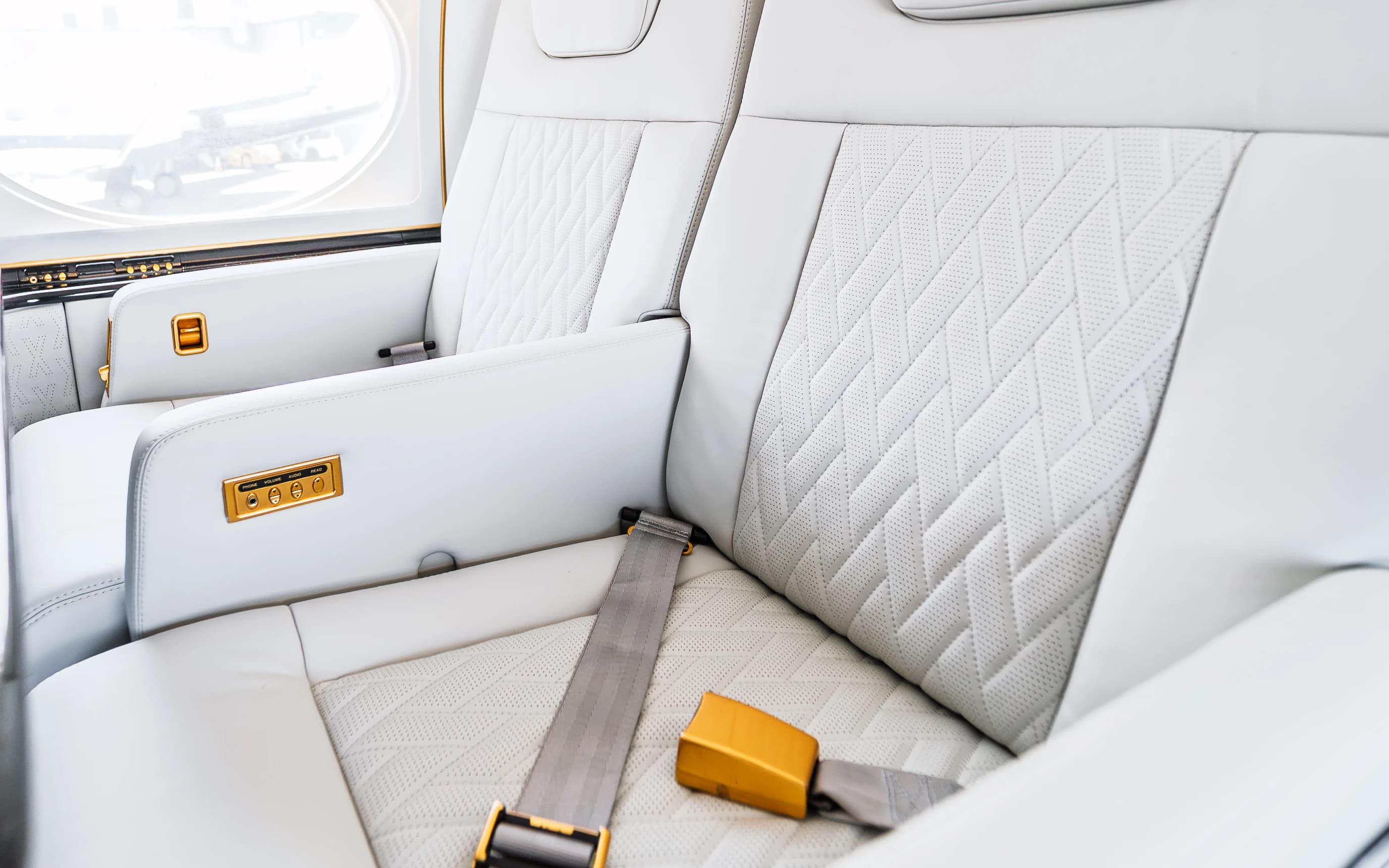 Gulfstream G550 upholstery detail with original perforations, shaped stitched panels, seat belt and gold-tone armrest controls.