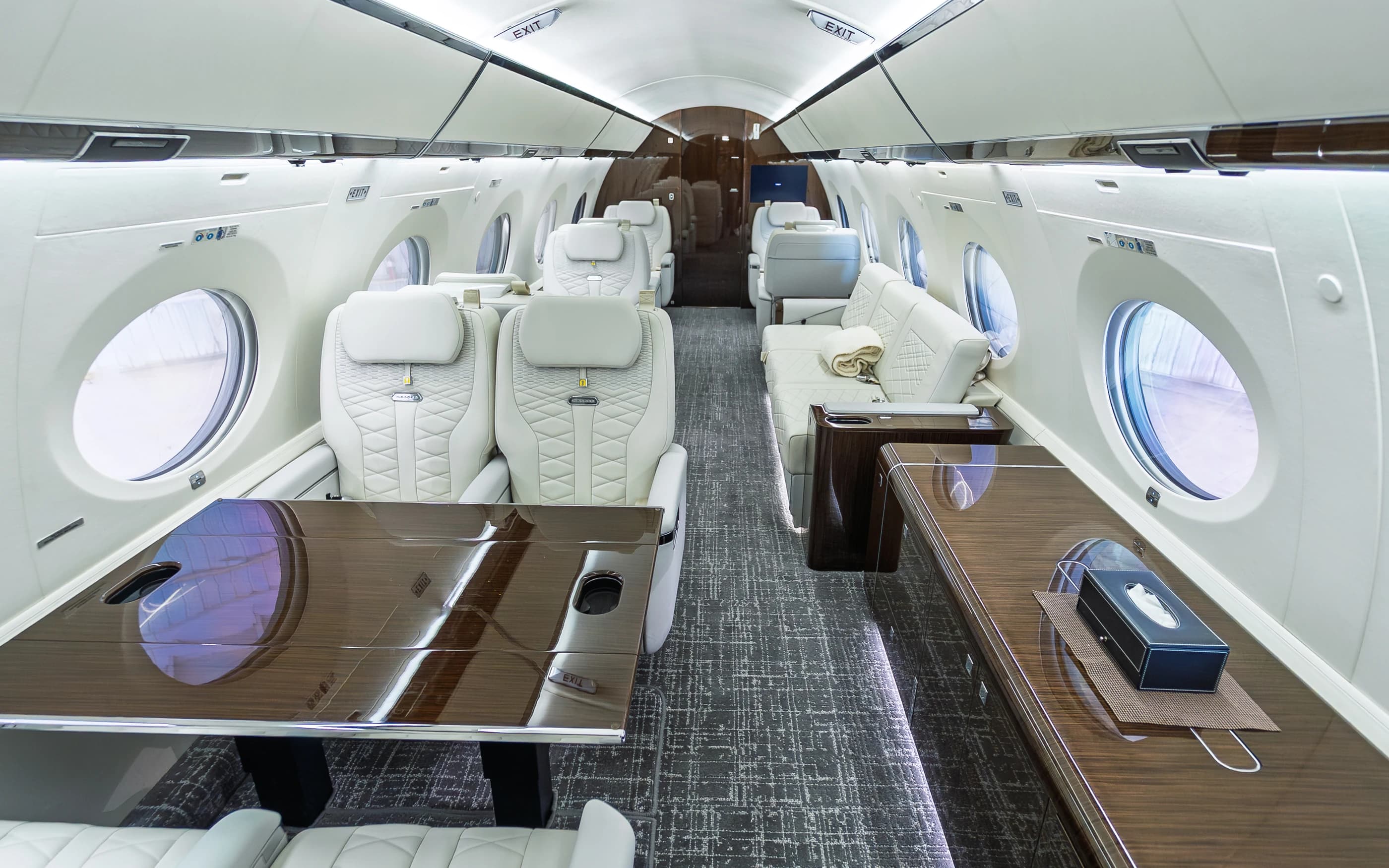 Gulfstream G650ER seating groups, wood-toned table and gray patterned carpet in the original cabin.