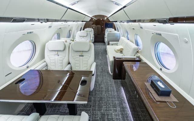 Gulfstream G650ER seating groups, wood-toned table and gray patterned carpet in the original cabin.
