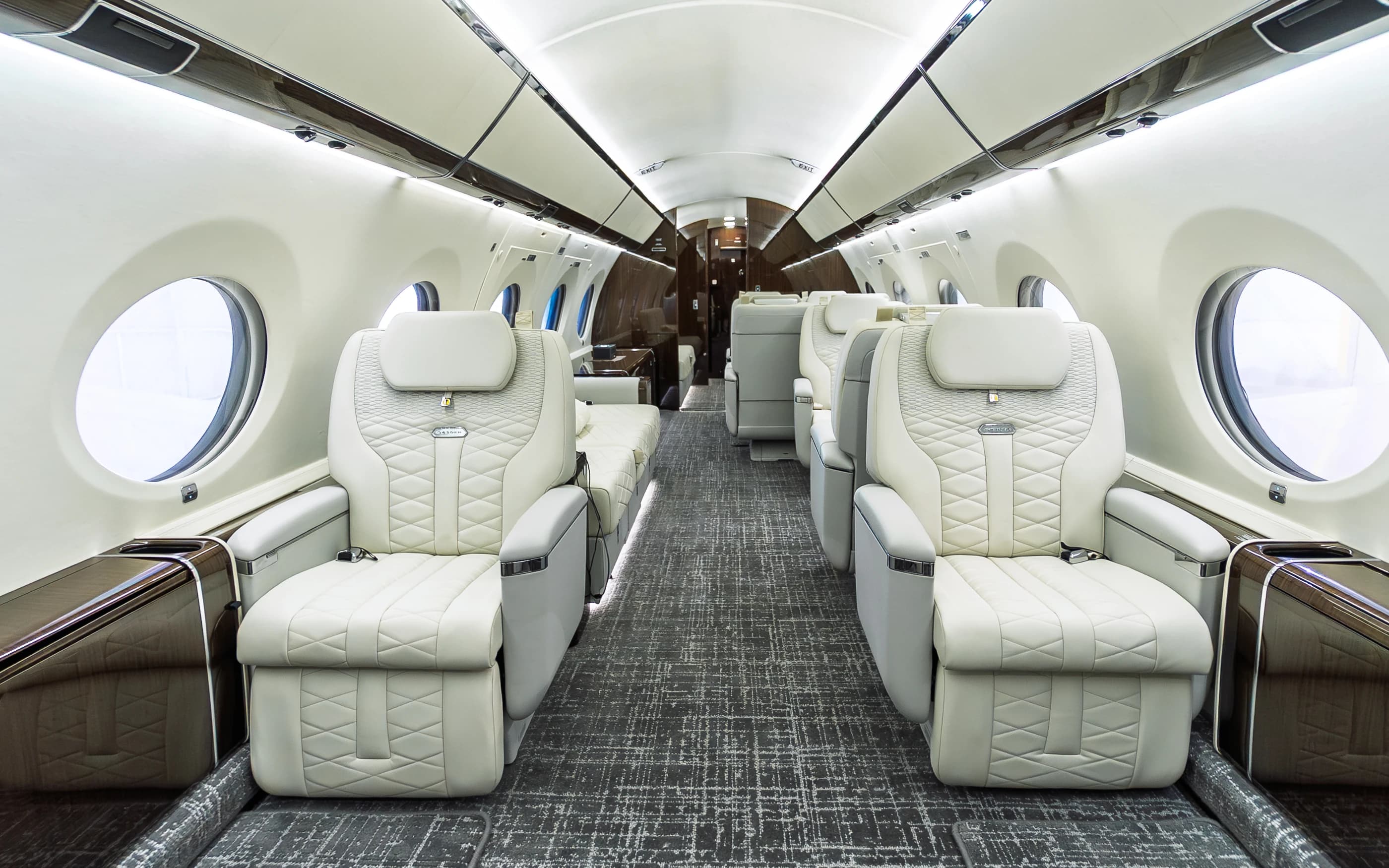 Centered Gulfstream G650ER cabin with original ivory seats, wood-toned side ledges and gray patterned carpet.