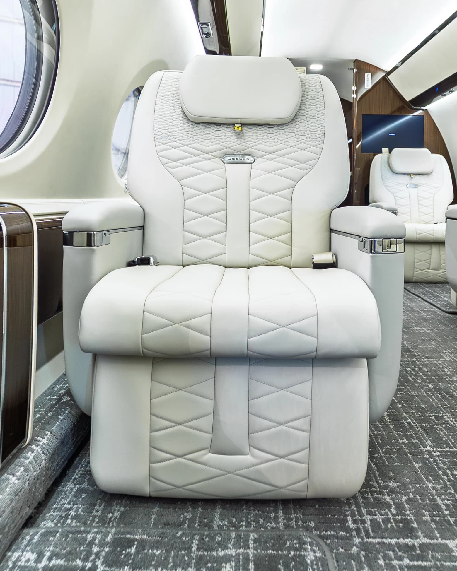 Frontal Gulfstream G650ER seat showing its original diamond quilting, metal badge and upholstered footrest.