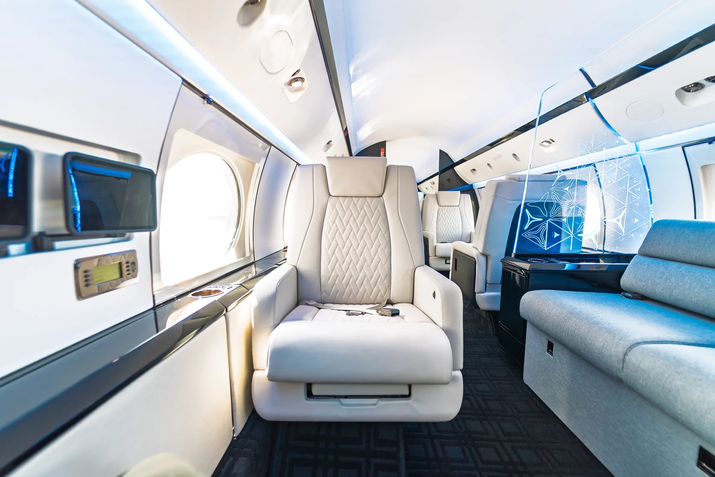 White Gulfstream G-IV seat beside the blue divan and illuminated cabin partition.