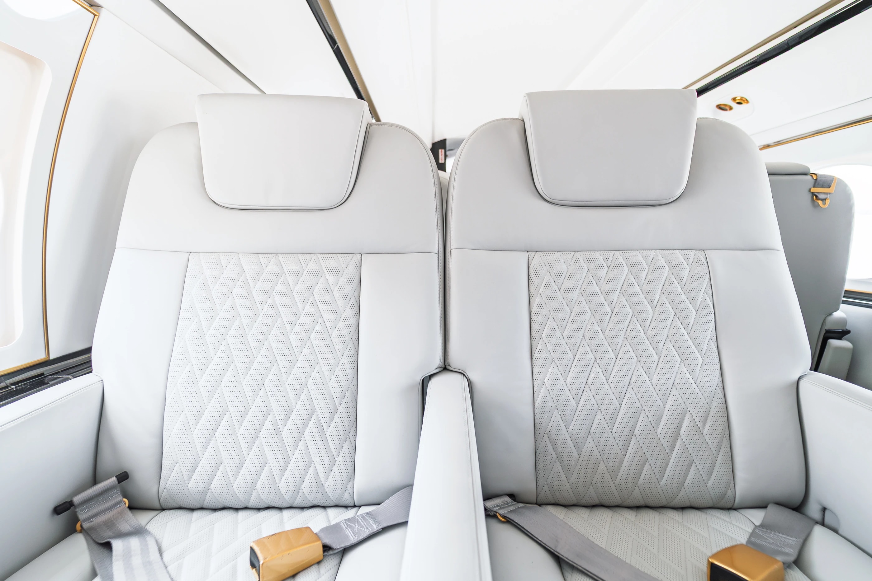 Paired Gulfstream G550 headrests and original perforated upholstery, with tailored stitching and gold-tone seat belt fittings.
