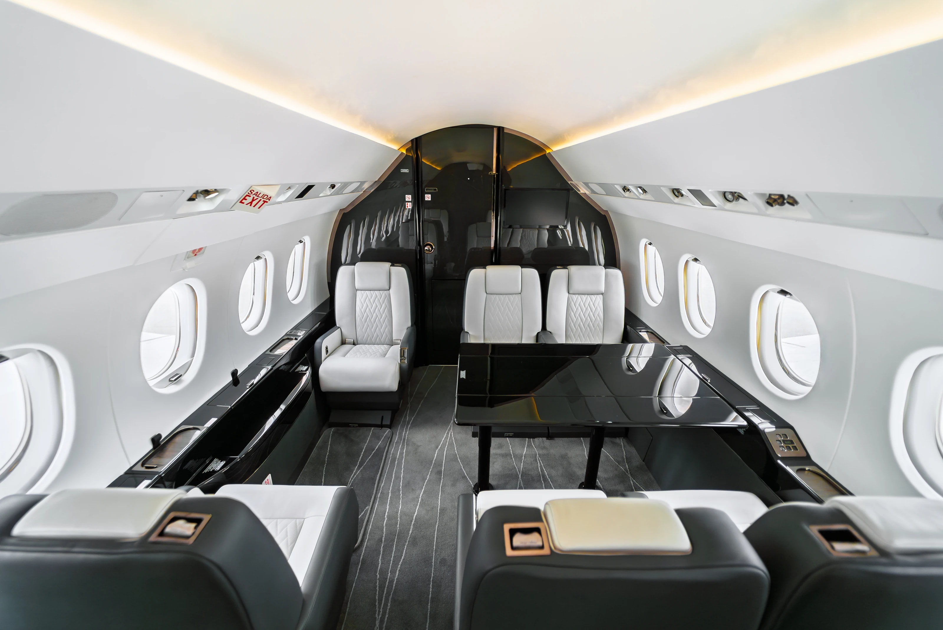 Wide Falcon 2000 cabin with club seating, glossy tables, dark cabinetry and warm ceiling lighting.