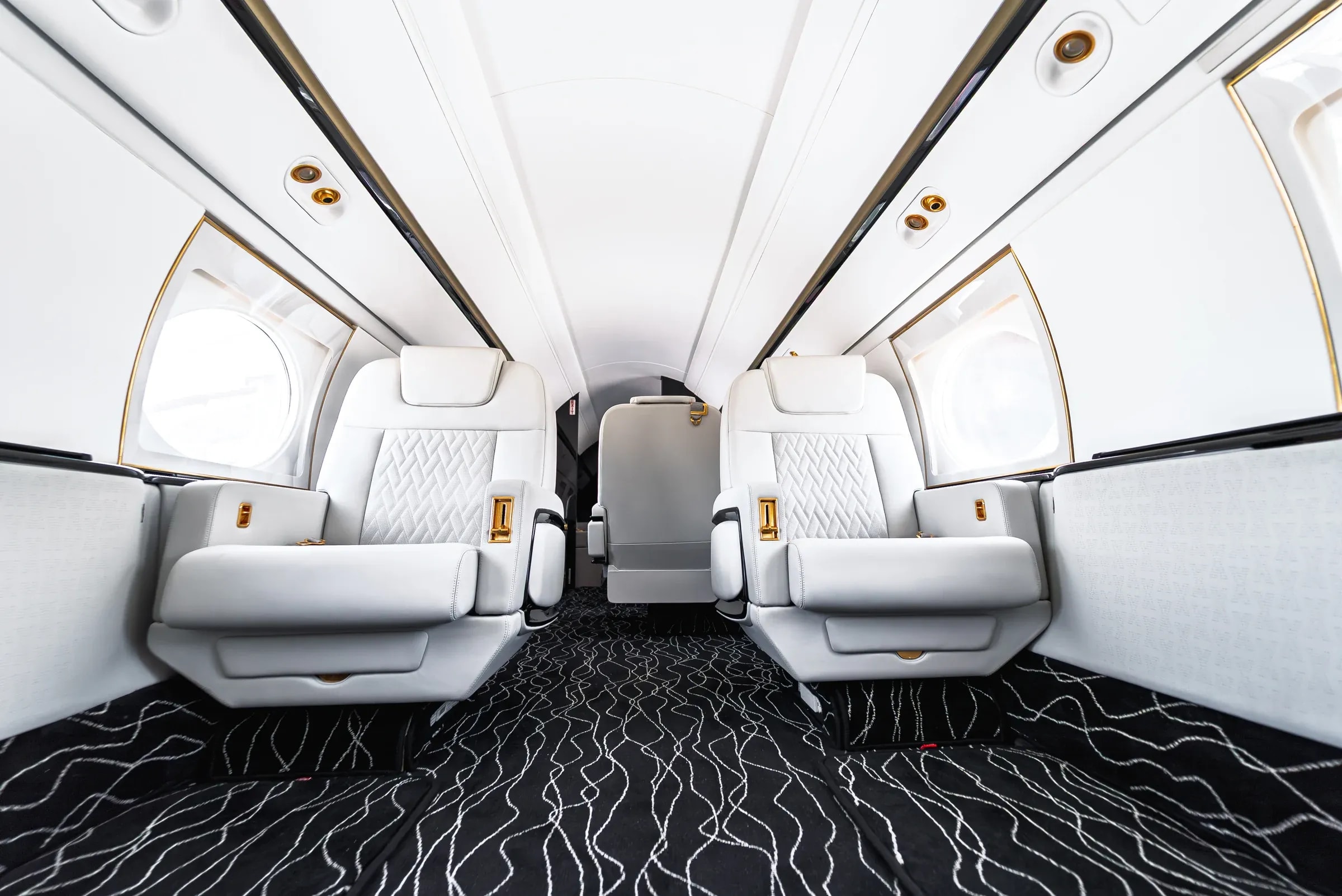 Low view of white Gulfstream G550 seats and the wavy patterned cabin carpet.