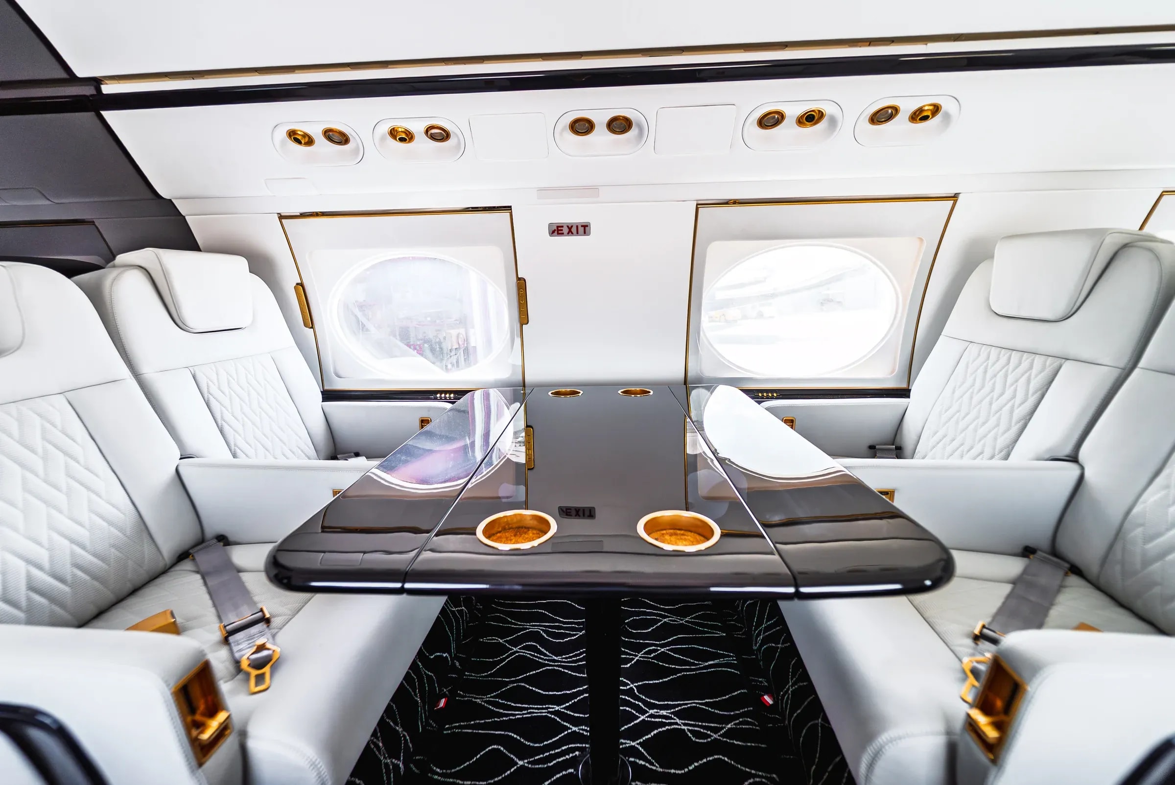 Facing Gulfstream G550 club seats around a glossy dark table with gold-tone cup holders.