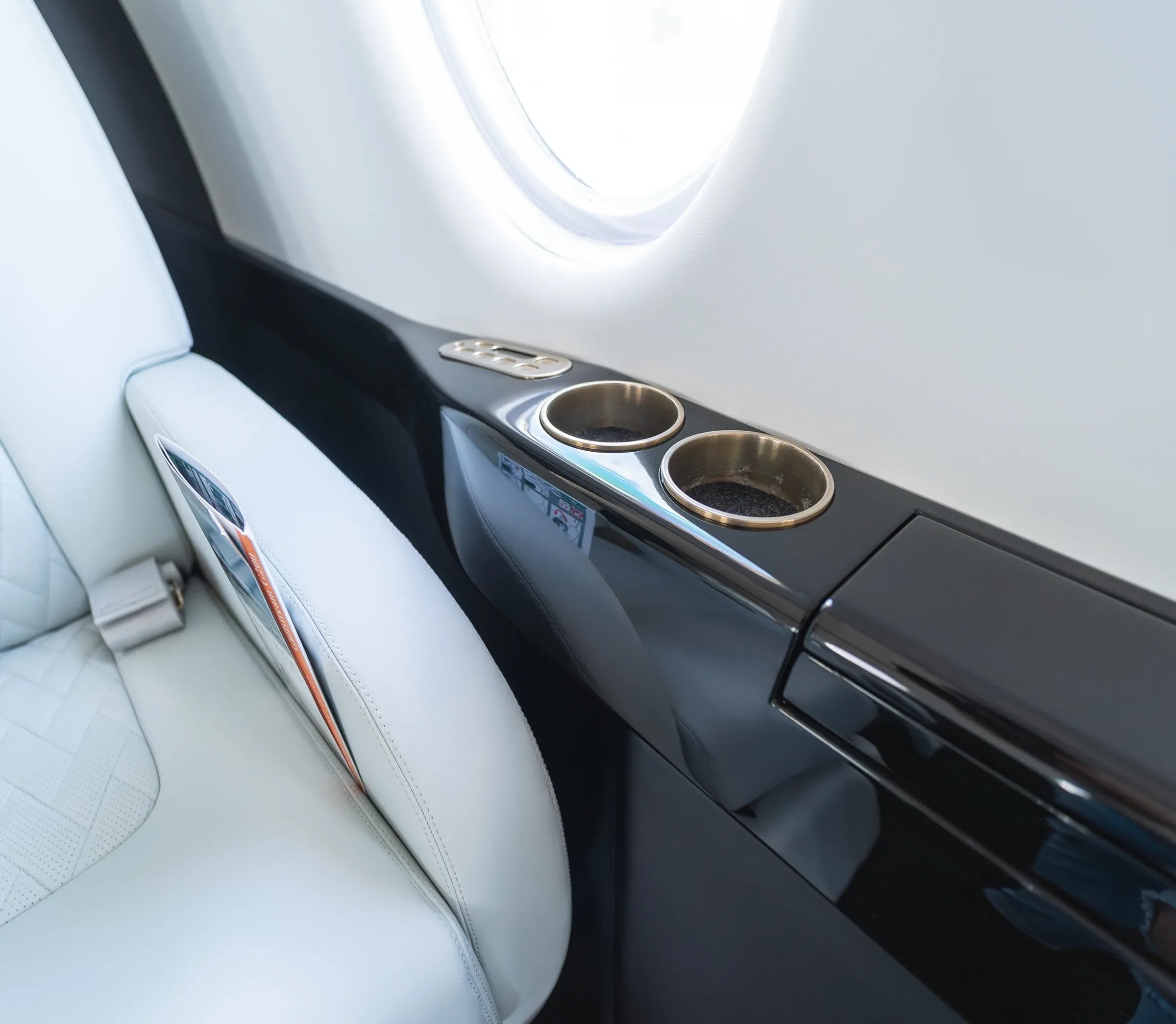 Glossy dark side ledge with cup holders beside a white Gulfstream G200 armrest.
