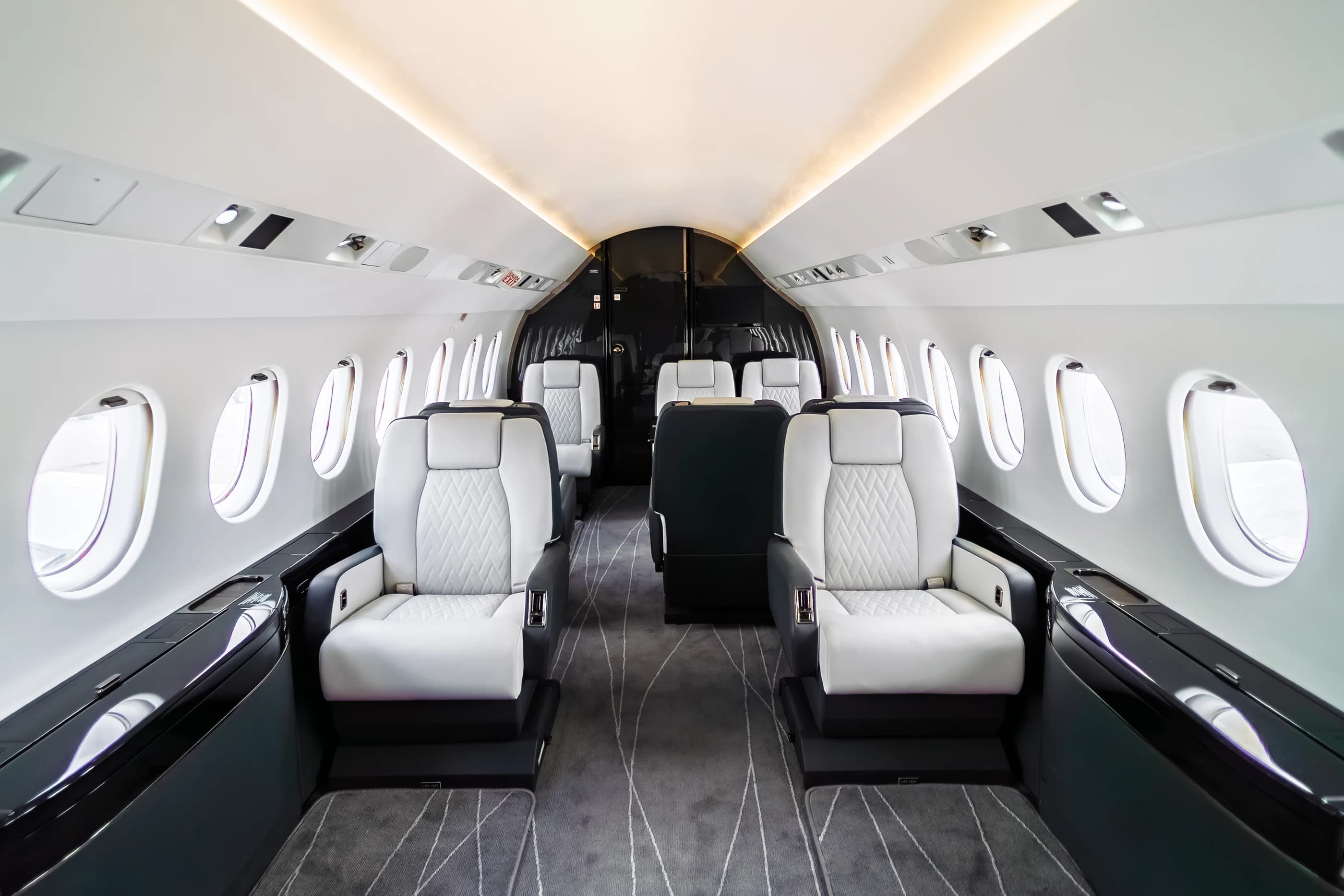 Falcon 2000 cabin with ivory quilted seating, dark surrounds and warm overhead lighting.