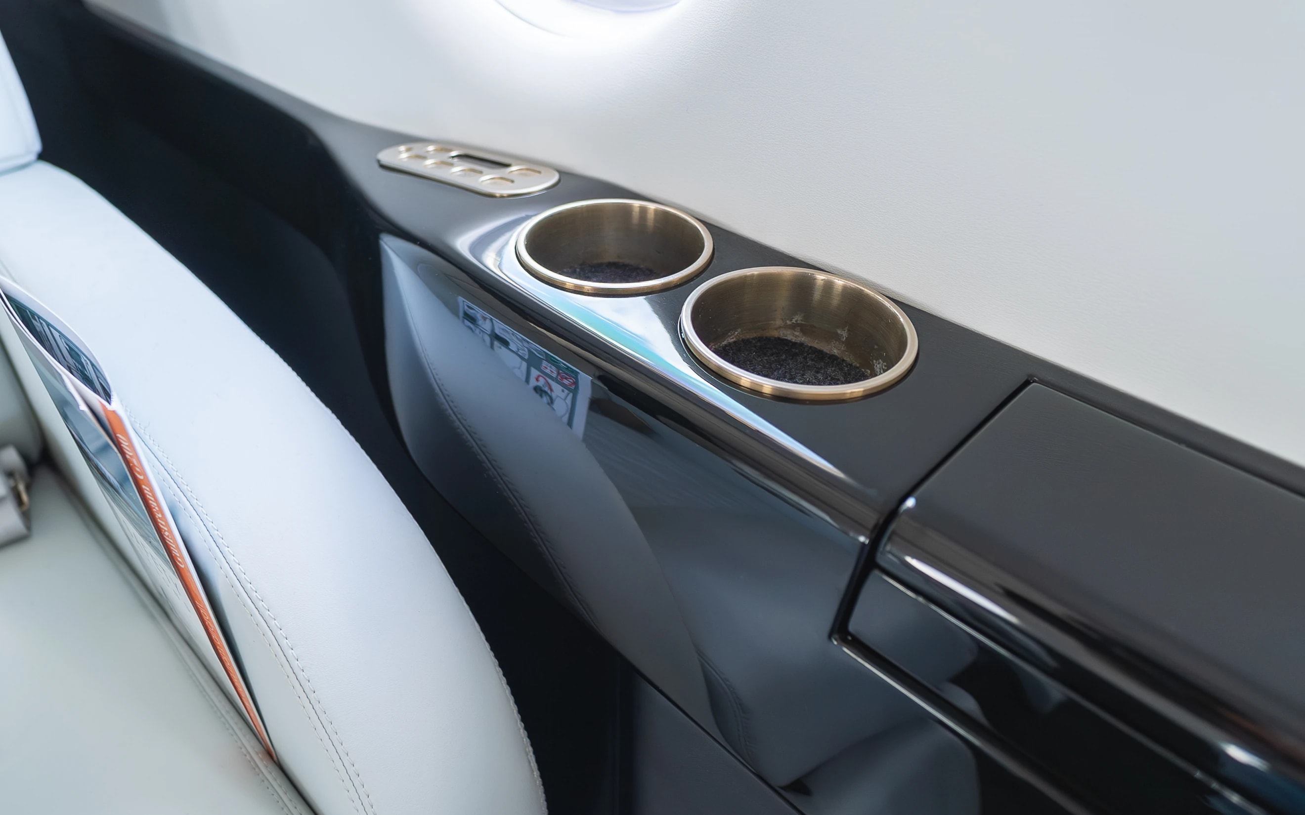 Gulfstream G200 glossy dark side ledge with original metal cup holders beside an ivory upholstered armrest.