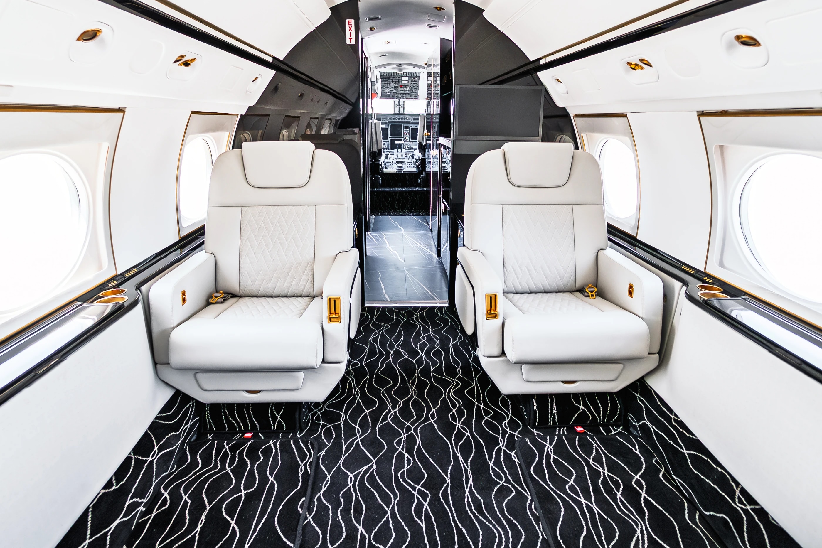 Paired Gulfstream G550 ivory seats, original quilted inserts and a flowing patterned carpet beside the forward cabin entrance.
