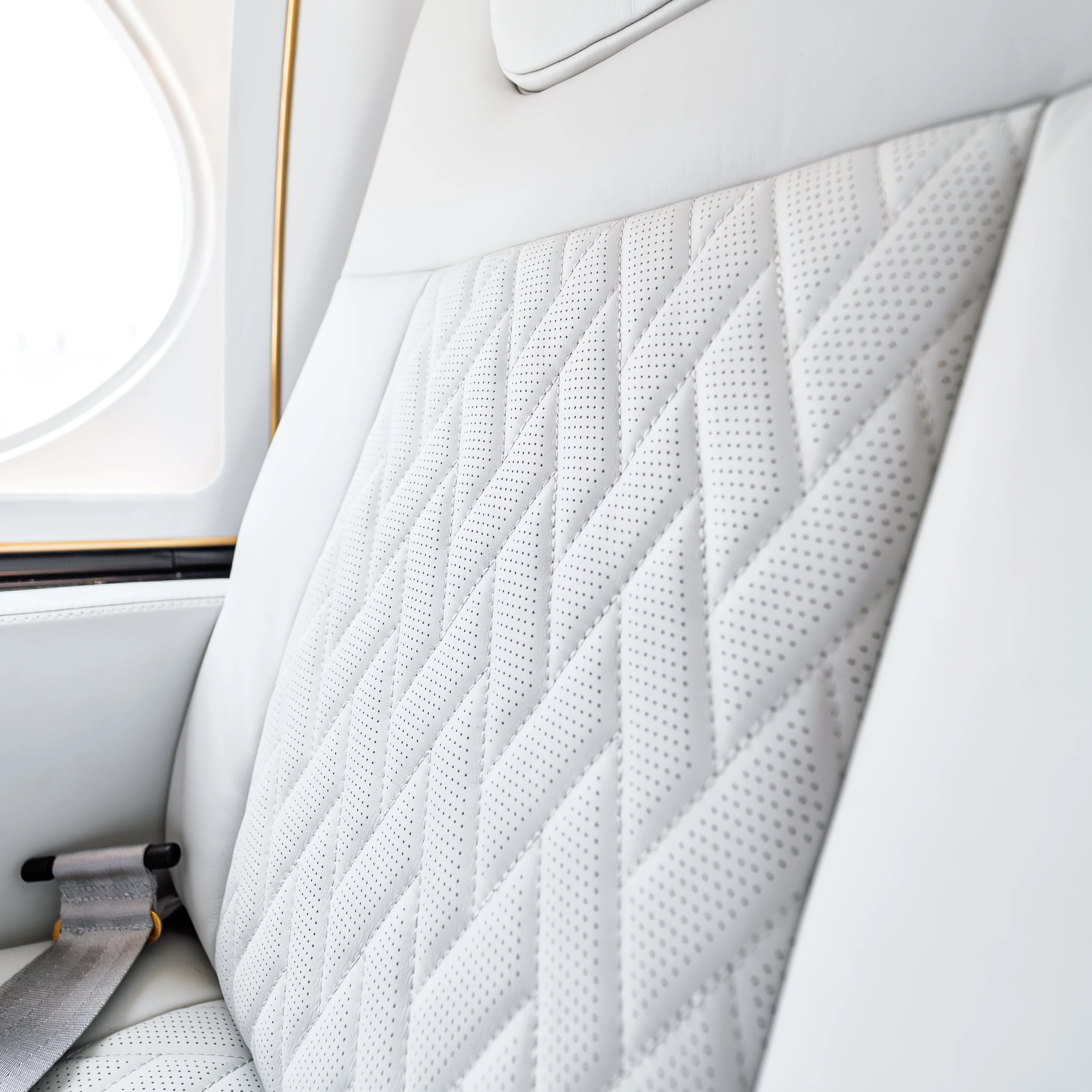 Original perforations and tailored stitching on Gulfstream G550 ivory upholstery beside a cabin window.