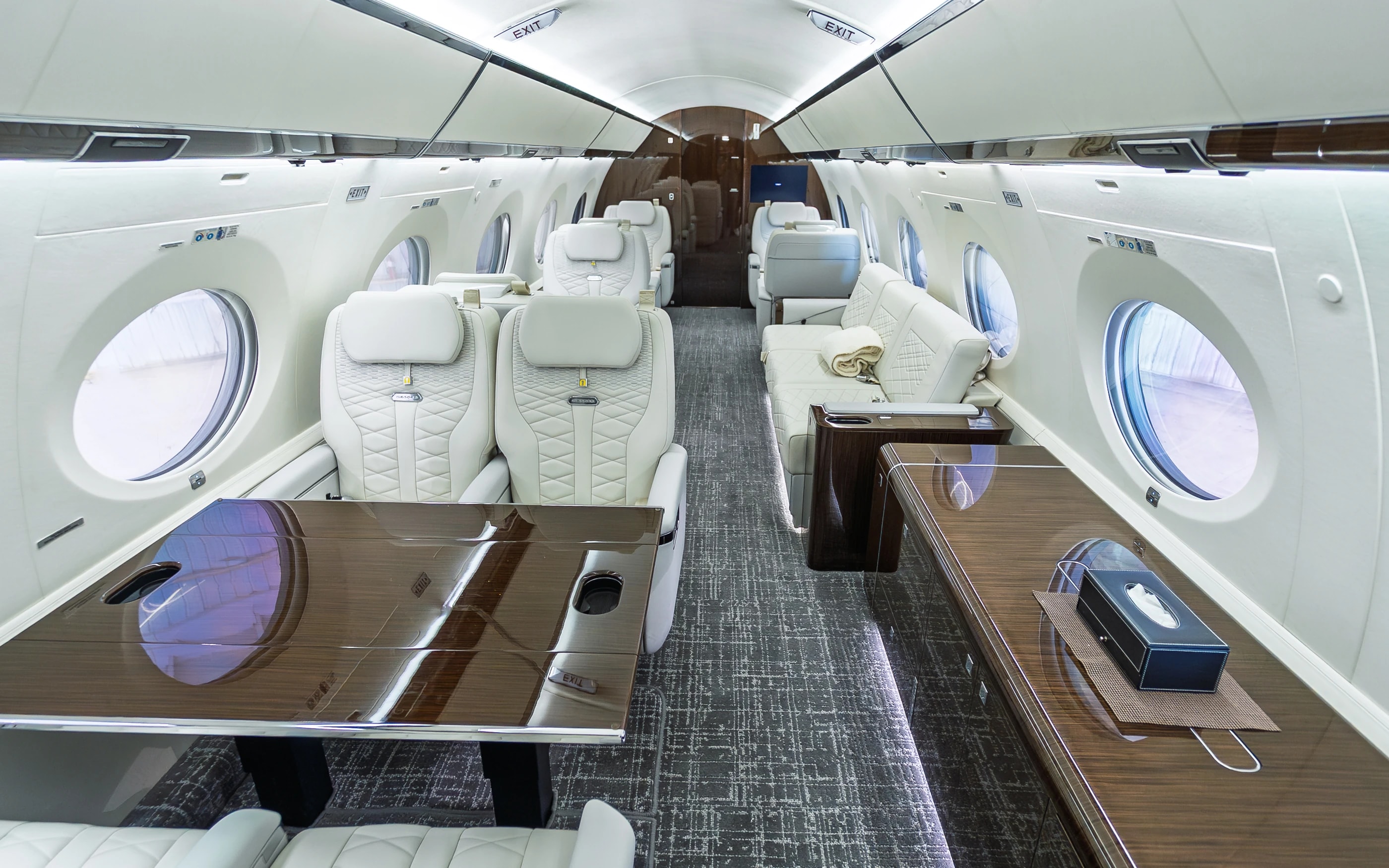 Gulfstream G650ER seating groups, wood-toned table and gray patterned carpet in the original cabin.