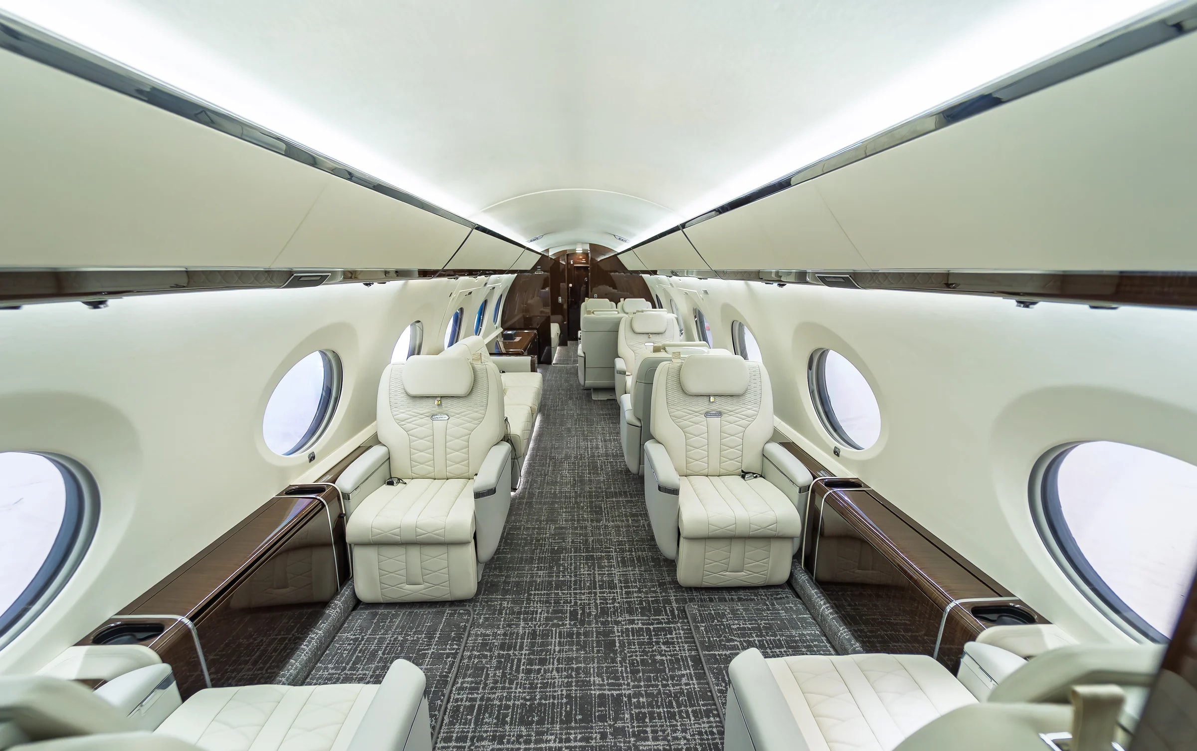 Centered Gulfstream G650ER cabin view with ivory quilted seats, glossy wood side ledges and gray patterned carpet.